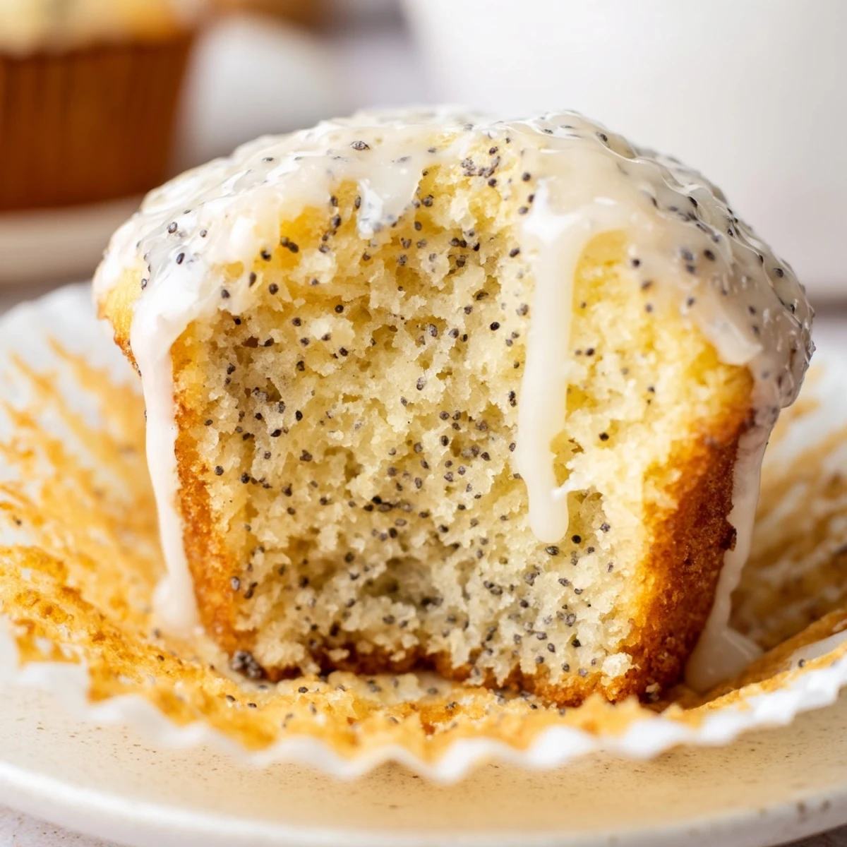 Freshly baked Lemon Poppy Seed Muffins with Yogurt sit on a cooling rack, showcasing golden tops and a moist crumb. Twelve golden-brown muffins fill a muffin tin, speckled with poppy seeds and a hint of lemon zest visible. A glass bowl of Greek yogurt and a halved lemon sit beside freshly baked Lemon Poppy Seed Muffins.