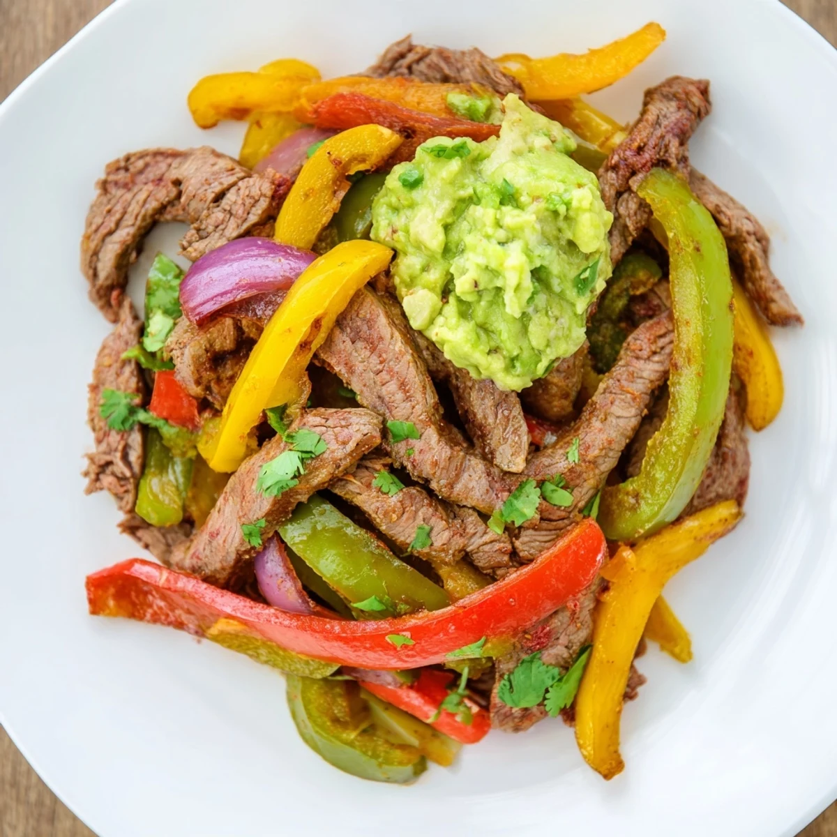 Tender marinated beef strips alongside colorful bell peppers and onions, served warm with flour tortillas and creamy guacamole on the side.