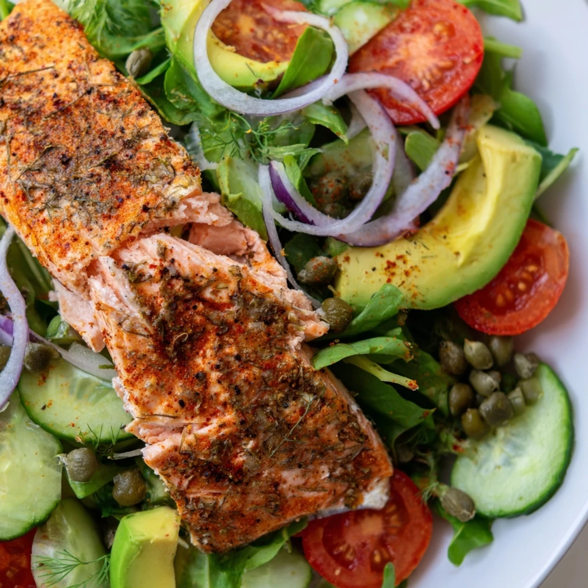 Tender baked salmon sits atop a bed of mixed greens, avocado, and red onion for a vibrant, healthy Baked Salmon Lunch Salad.