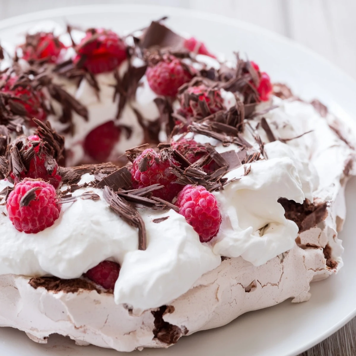 A slice of chocolate raspberry pavlova with crisp meringue layers and fresh berries on a white plate.