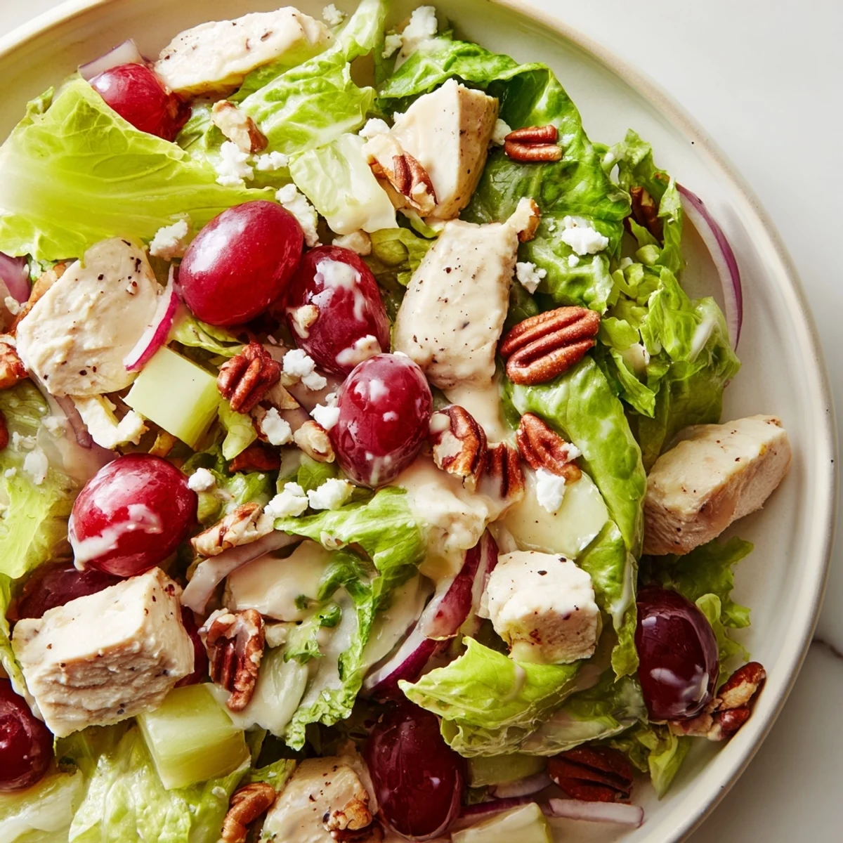 A vibrant Chicken Pecan Salad with Dressing served on a white plate, featuring red onion and feta for extra color and flavor.  