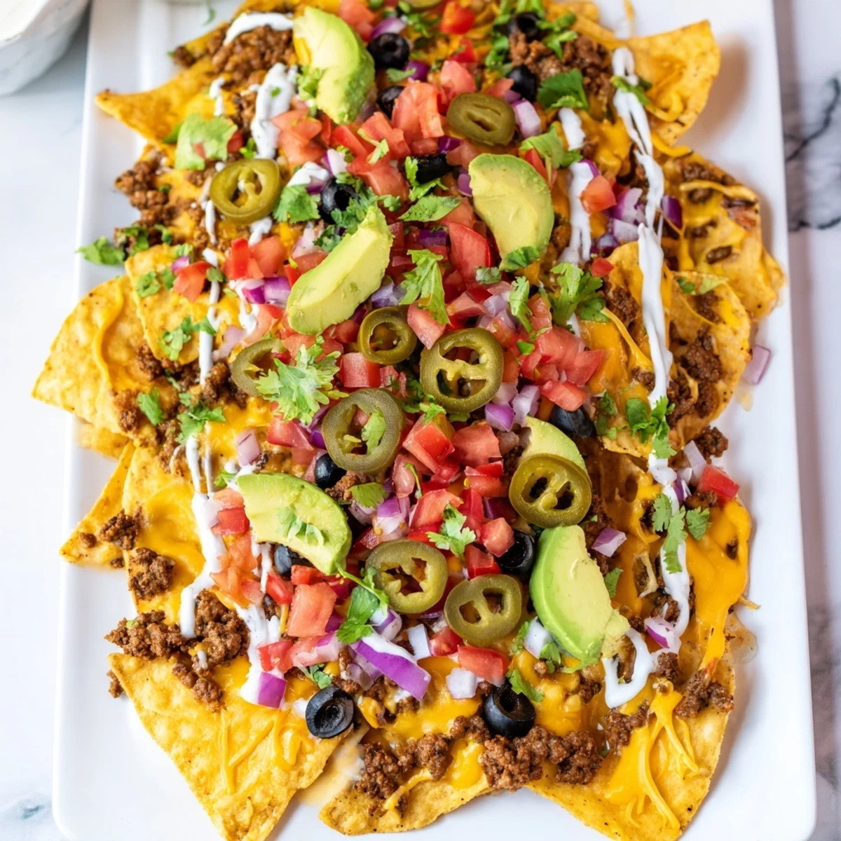 A steaming Super Bowl Nacho Platter with seasoned beef, melted cheddar, and fresh toppings on crispy tortilla chips.