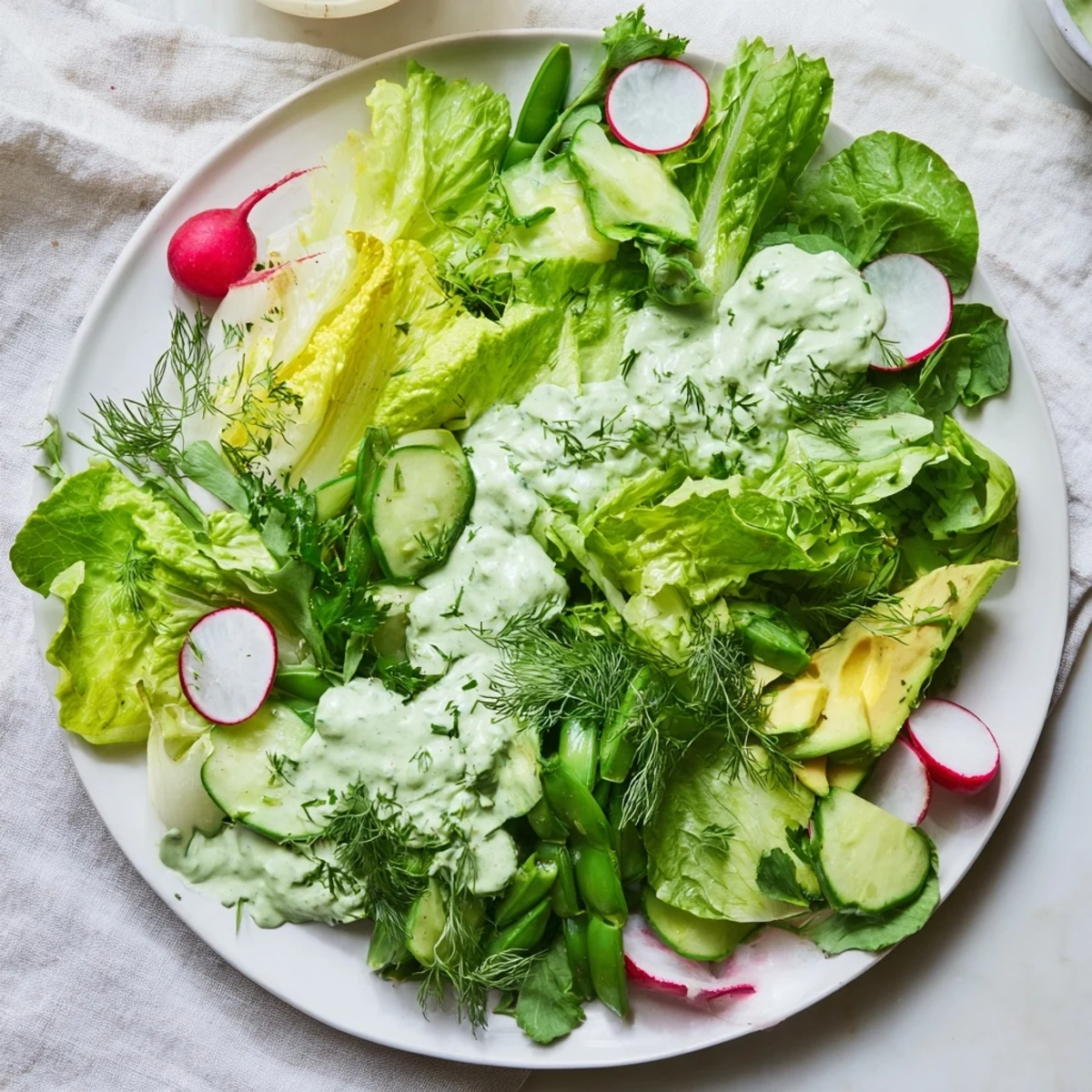 An inviting serving of Green Salad with Green Goddess Dressing, drizzled generously over mixed greens, cucumber slices, and creamy avocado for a light meal.