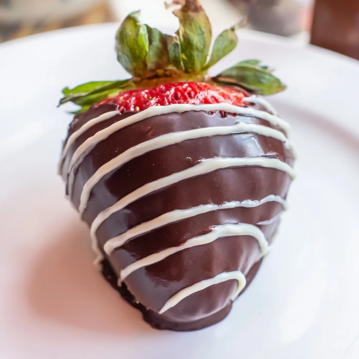 A close-up of glossy chocolate dipped strawberries with white chocolate drizzle, highlighting juicy red fruit and rich dark chocolate coating.