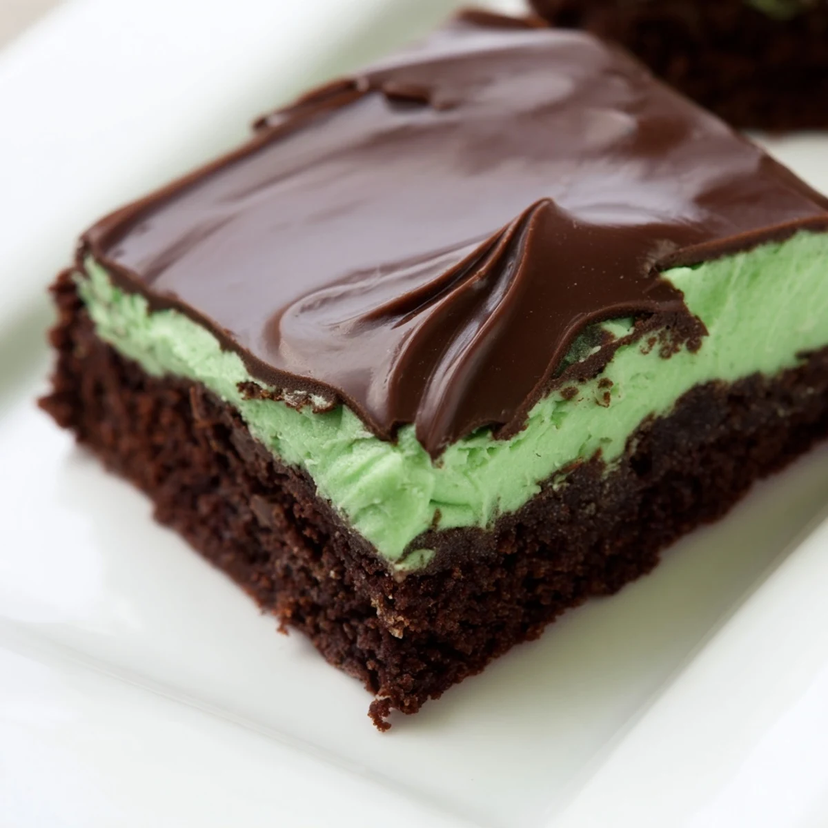 Green Mint Brownies cut into squares show a fudgy texture, a bright mint swirl, and glossy chocolate glaze on a rustic plate.