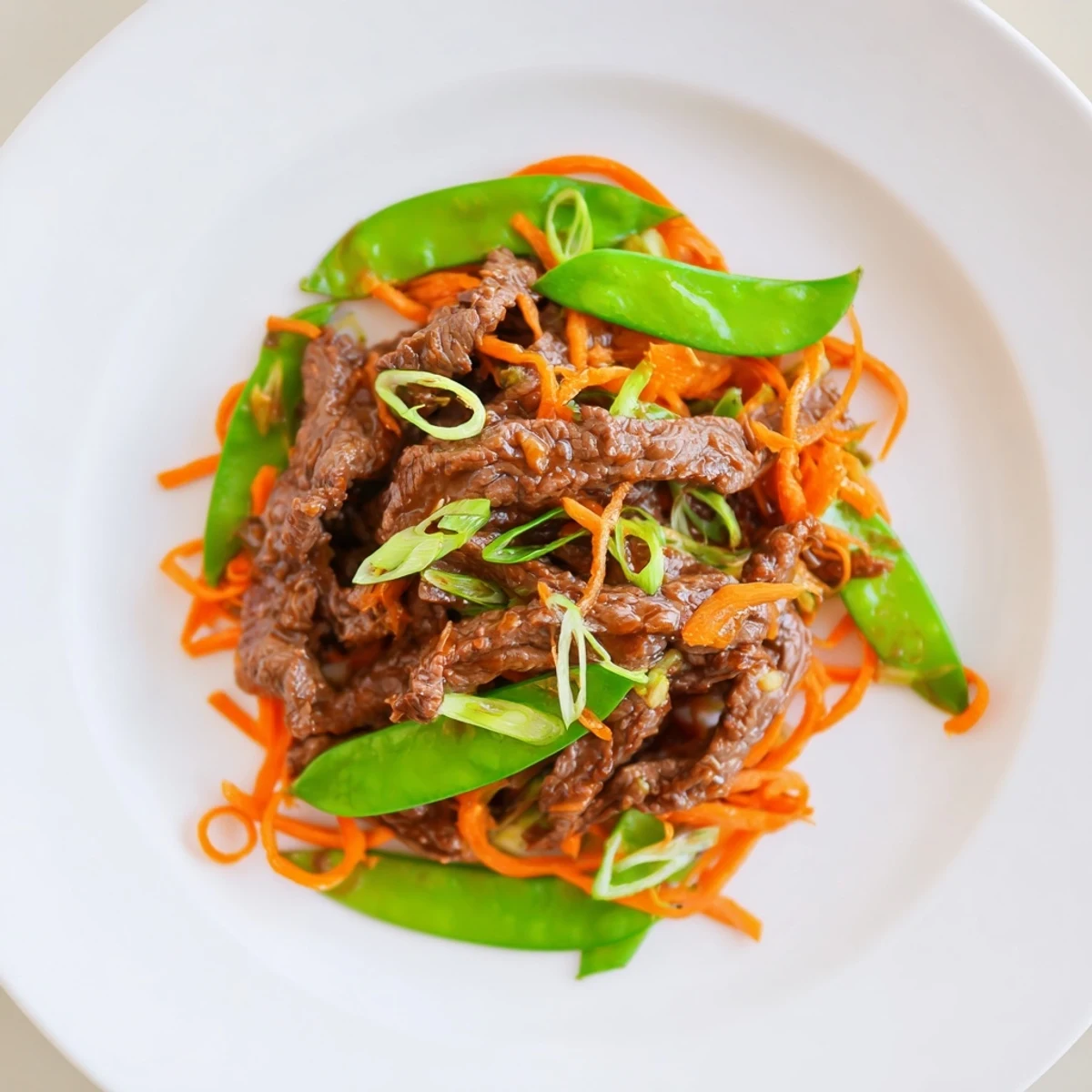 A close-up of Beef Stir Fry with Snow Peas and Carrots, highlighting juicy beef and vibrant orange carrots on a plate.