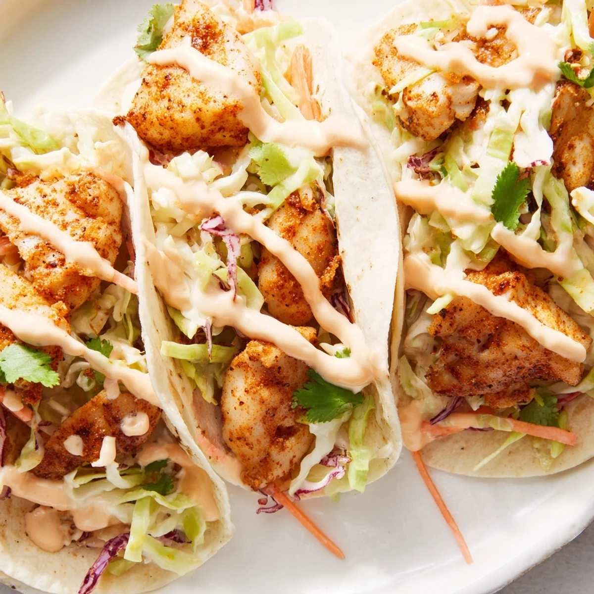 Fresh lime wedges and a drizzle of creamy sauce accent these Cajun Spiced Fish Tacos.