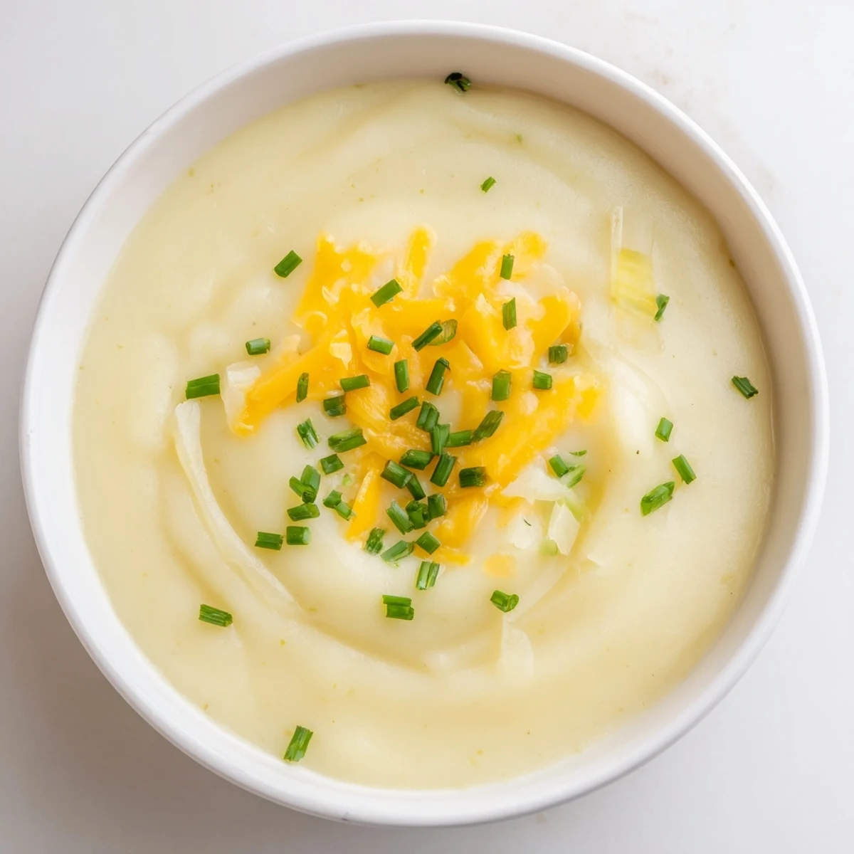Creamy Irish Potato Leek Soup with Sharp Cheddar, garnished with chives, served steaming hot in a rustic bread bowl.