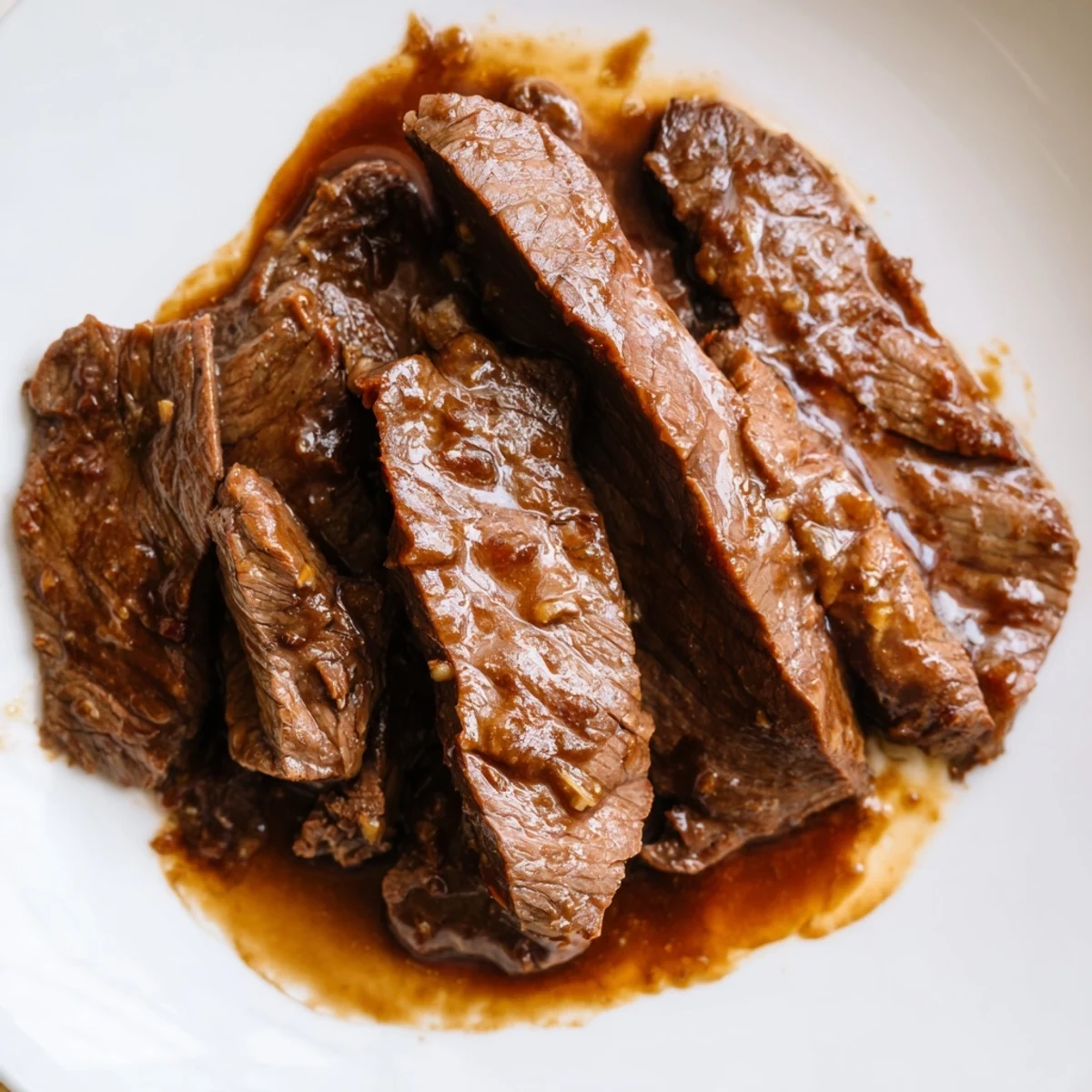 Tender slices of Ultimate Slow Cooker Mongolian Beef glazed in a sweet, savory sauce served over steamed rice in a bowl.