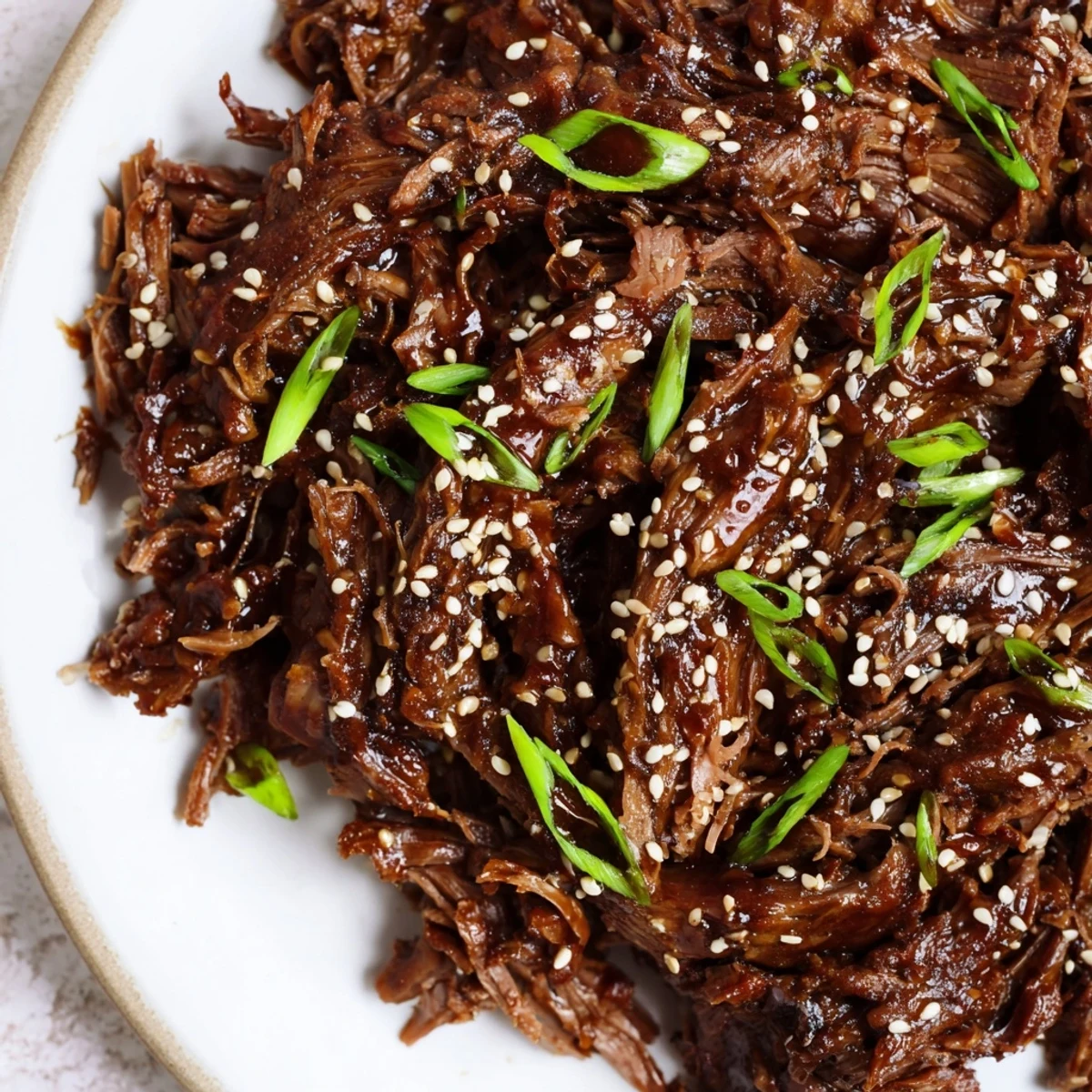 Close-up of juicy Crock Pot Korean Beef chunks glistening with thick sauce, served on a plate with chopsticks and rice.