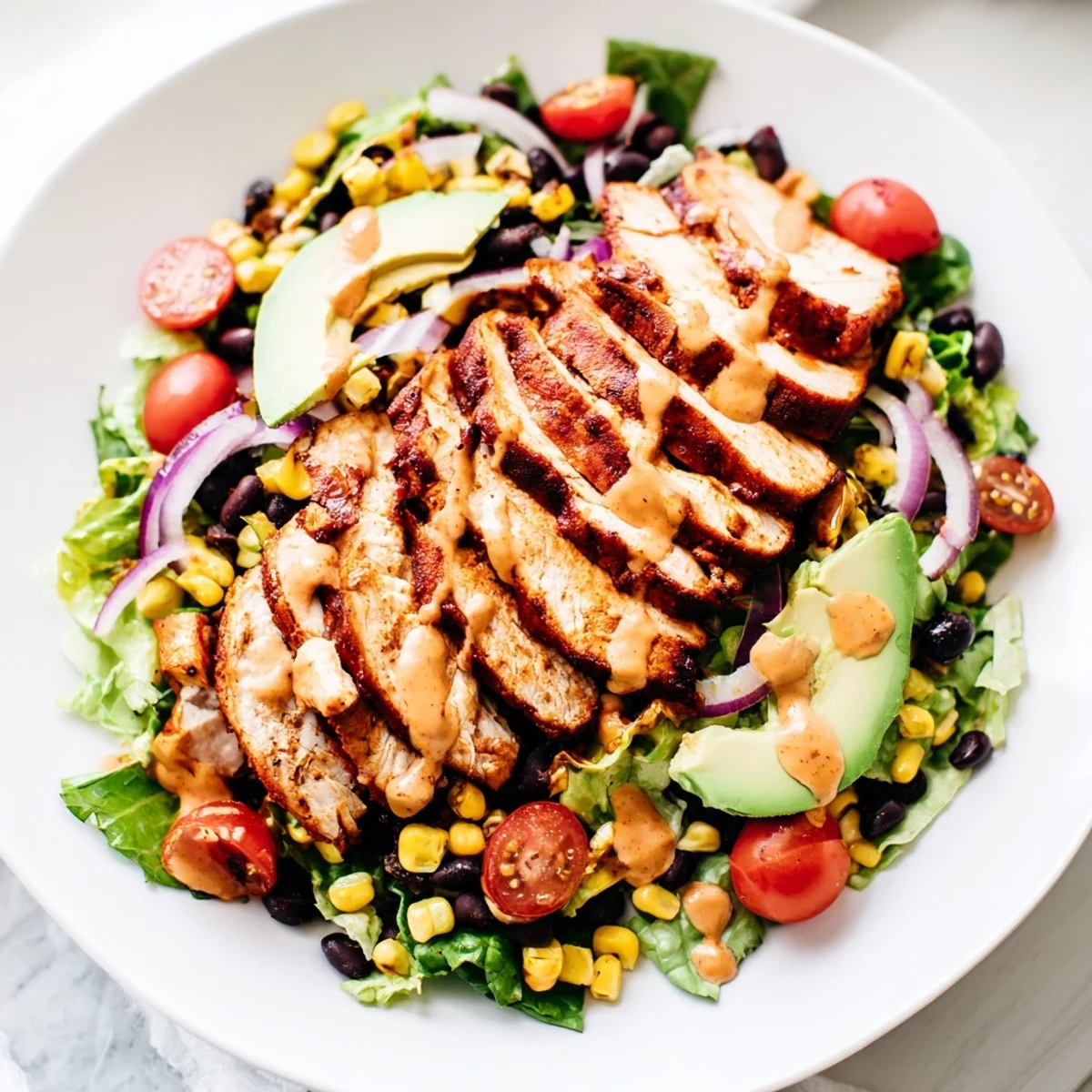 Sliced chipotle lime chicken salad on a bed of mixed greens, topped with avocado, black beans, and corn.