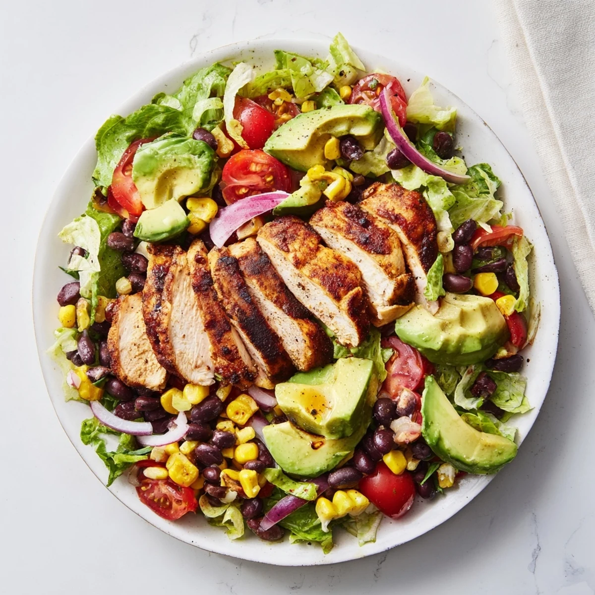 Close-up of chipotle lime chicken salad ingredients, featuring smoky chicken, crisp vegetables, and tangy dressing drizzle.