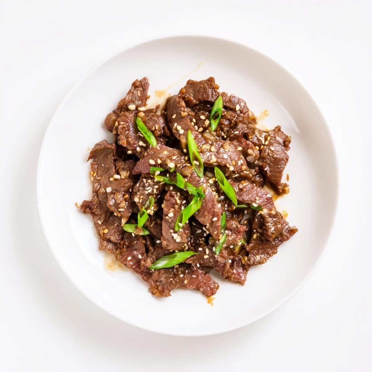 Steamed rice beside a bowl of Ultimate Slow Cooker Mongolian Beef, featuring tender beef strips coated in a glossy, savory-sweet sauce with green onions.