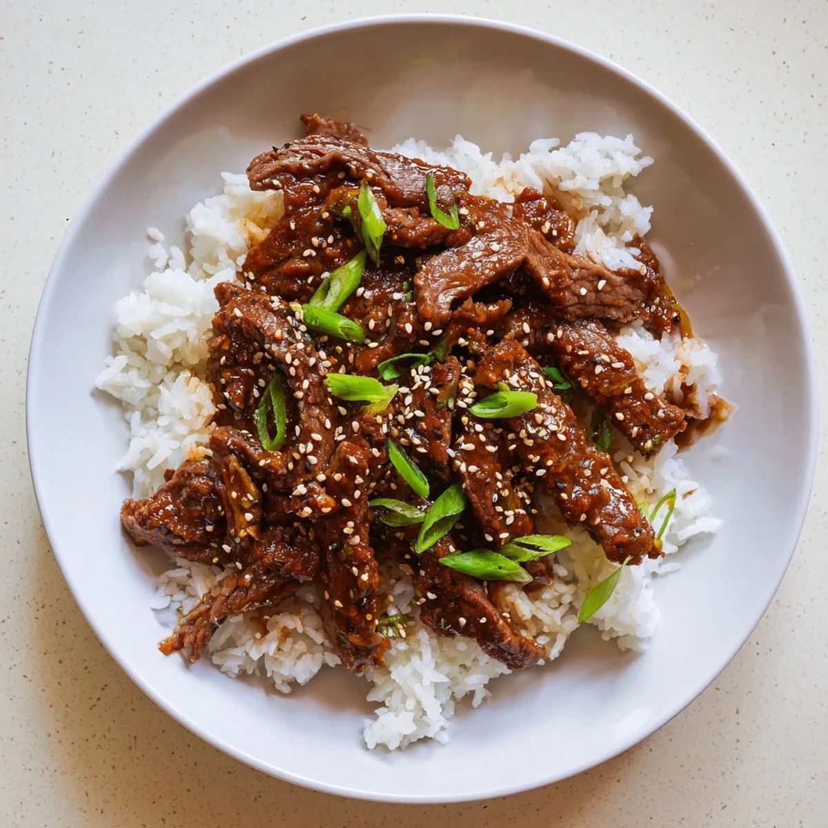 Ultimate Slow Cooker Mongolian Beef plated with vibrant green onions and a glossy, savory-sweet sauce.