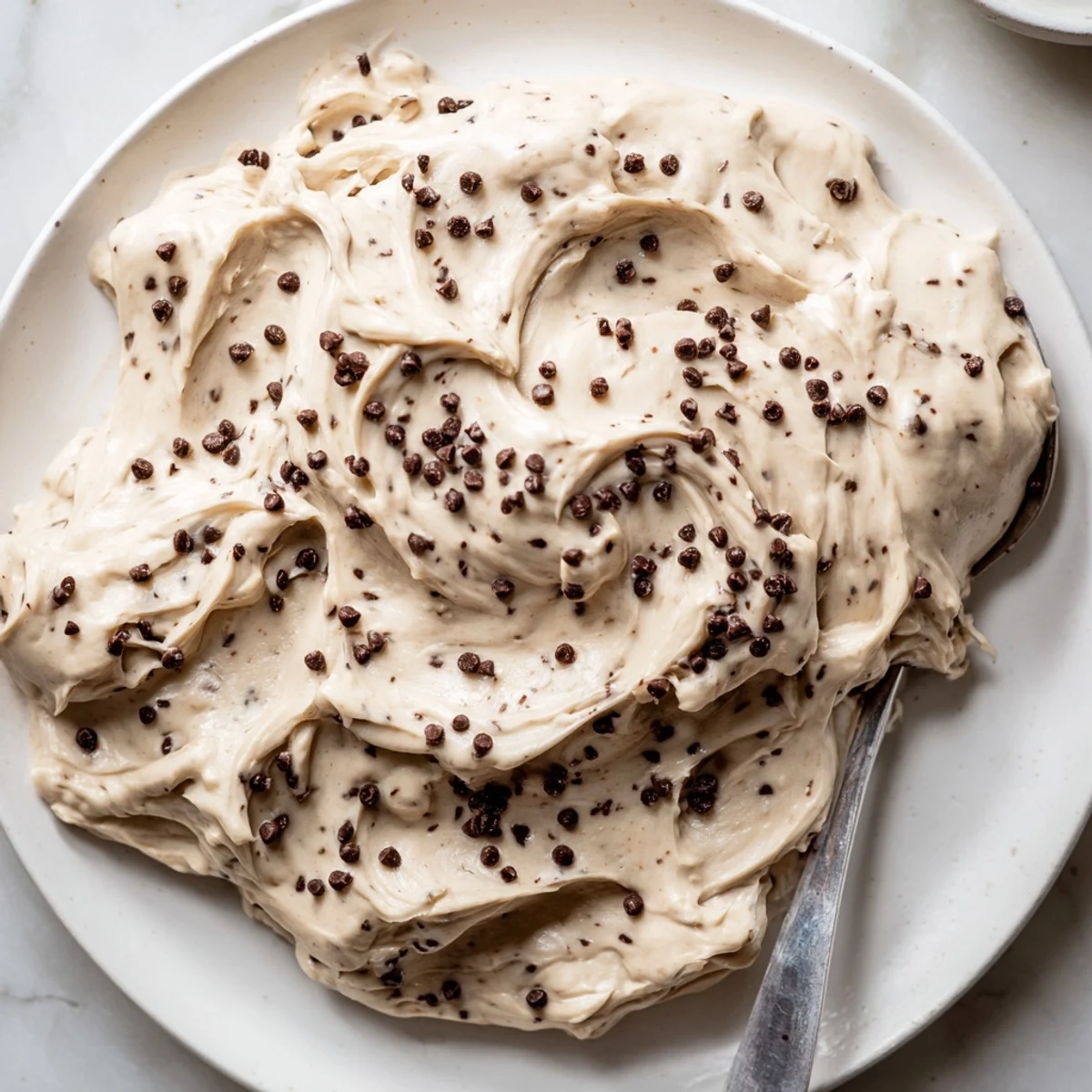 Spoonfuls of Cookie Dough Frosting show brown sugar flecks and chocolate chips for a rich dessert topping.