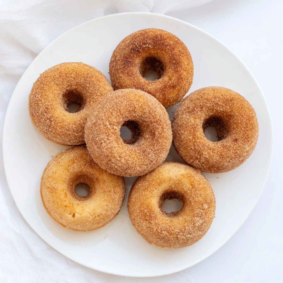 Warm Delicious Baked Cinnamon Sugar Donuts You Cant Resist sprinkled with sugar and cinnamon on a rustic wooden board.