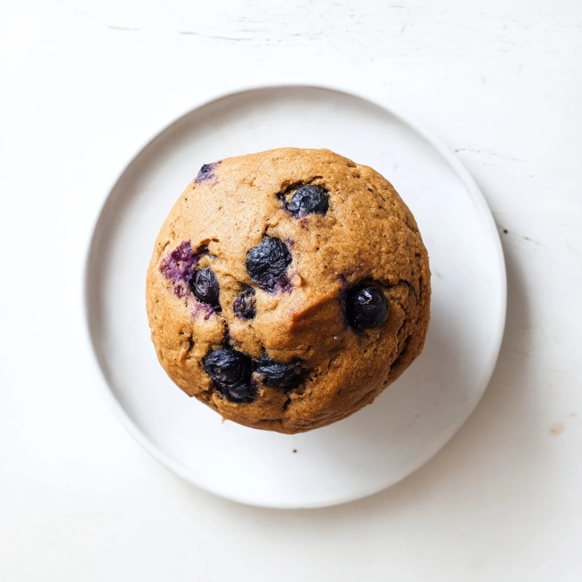 Freshly baked Greek Yogurt Blueberry Protein Muffins on a cooling rack with a bite taken out to reveal a moist, fluffy crumb studded with ripe berries.