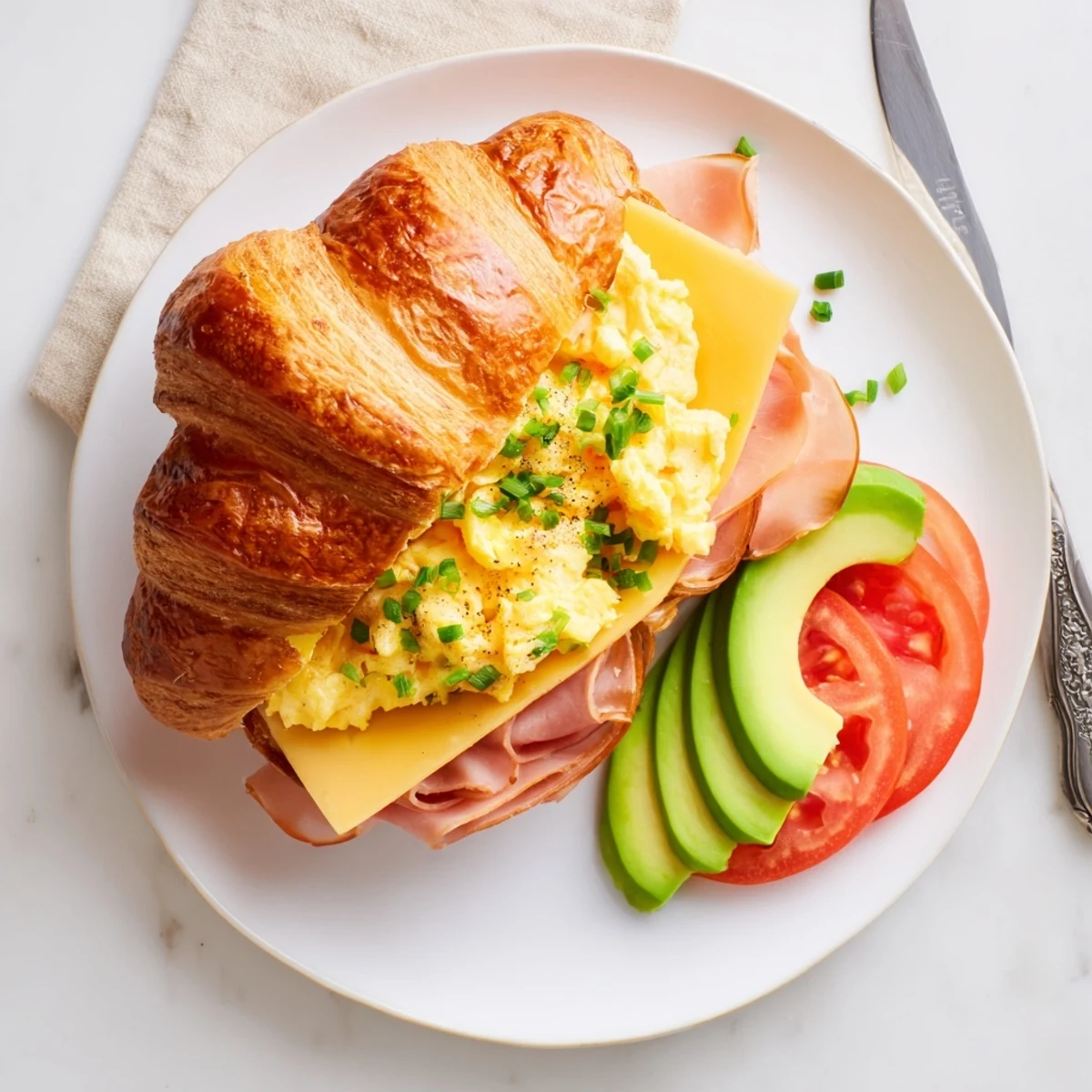 Warm Flaky Croissant Breakfast Sandwich served with sliced tomatoes and chives for breakfast.