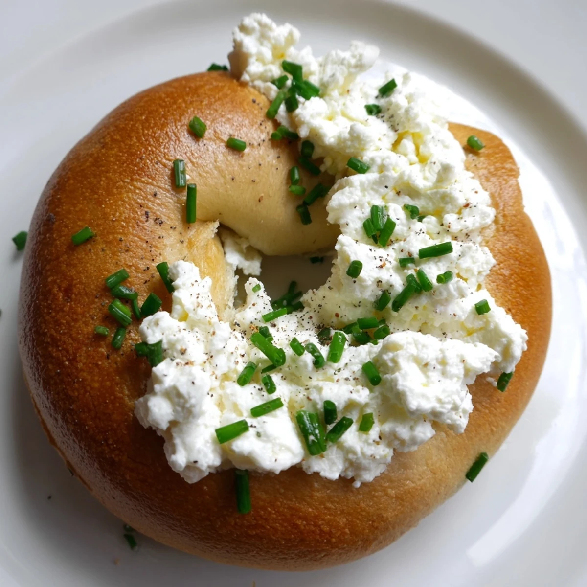 Warm Protein Bagels with Cottage Cheese sit beside a cup of coffee, topped with chives and black pepper for a savory breakfast.
