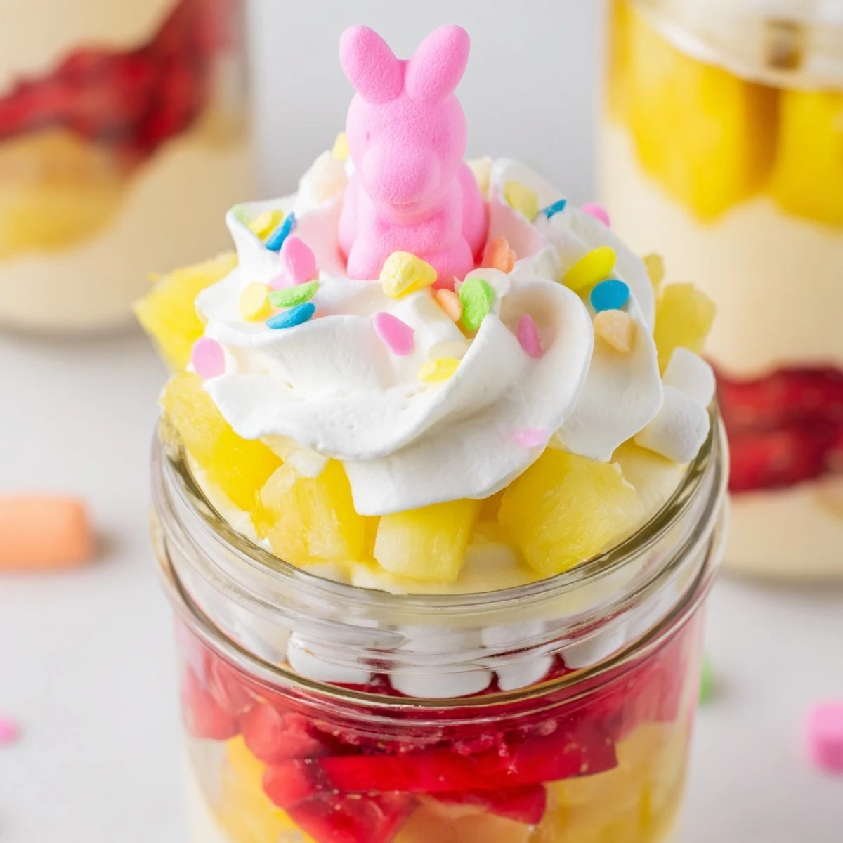 In a food photography style, the Jello Pie Easter Bunny Parfait In A Jar sits on a spring table, displaying a spoonful of the layered dessert being lifted out to show its texture.