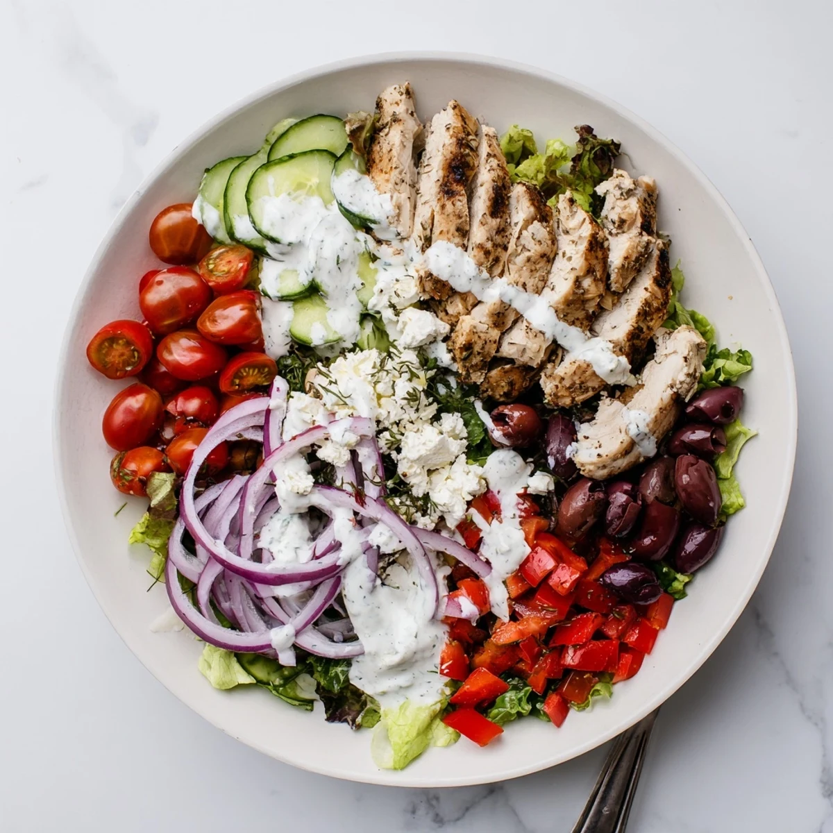Sliced grilled chicken breast on mixed greens with cucumber, tomatoes, and creamy tzatziki dressing for a refreshing Greek salad.