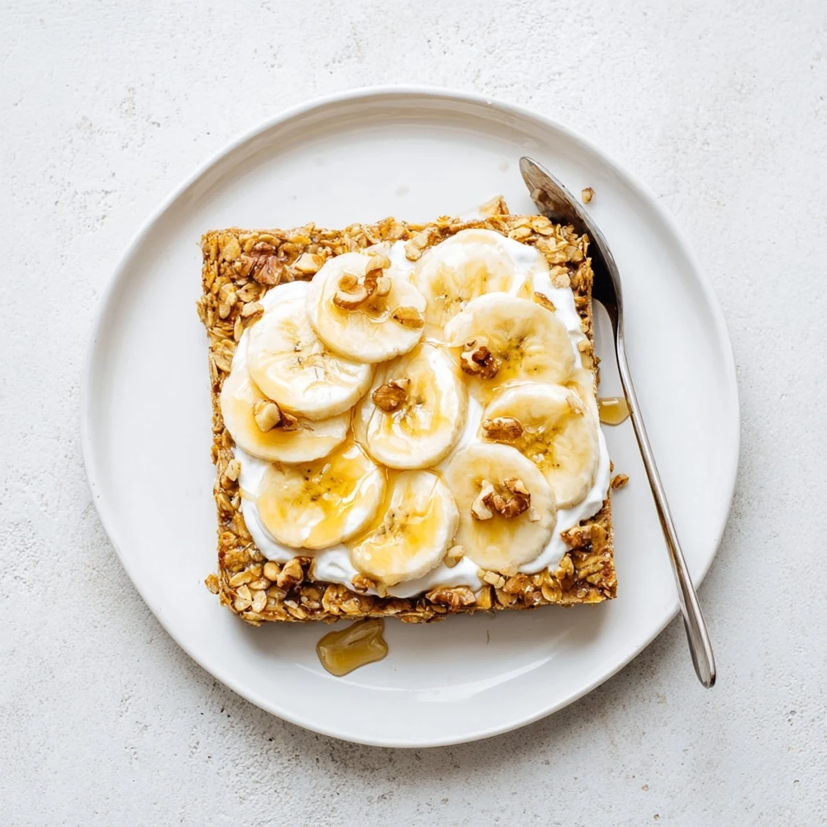 Warm Banana Baked Oatmeal with Greek Yogurt topped with fresh banana slices and maple drizzle.