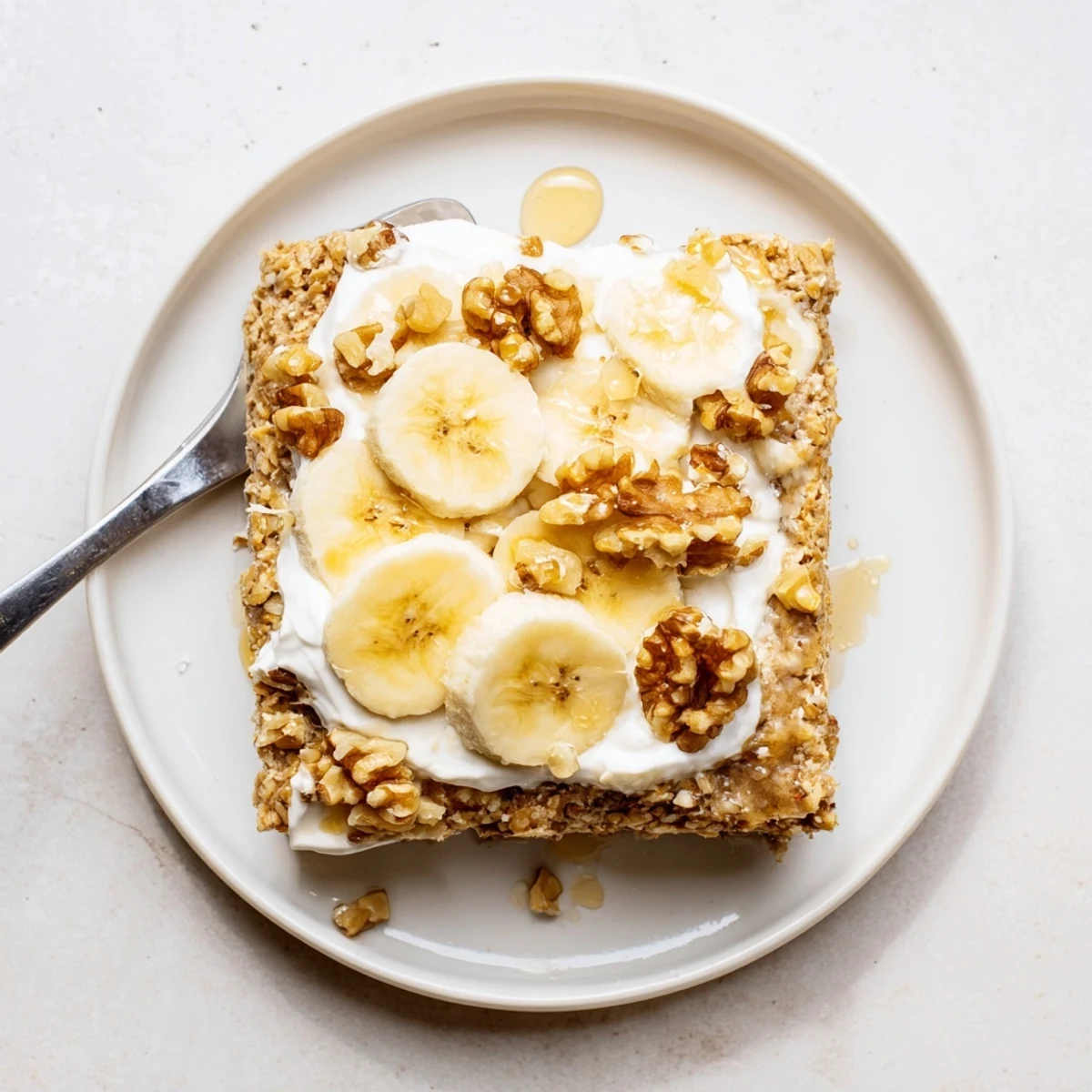 Banana Baked Oatmeal with Greek Yogurt on a plate with walnuts and honey nearby.