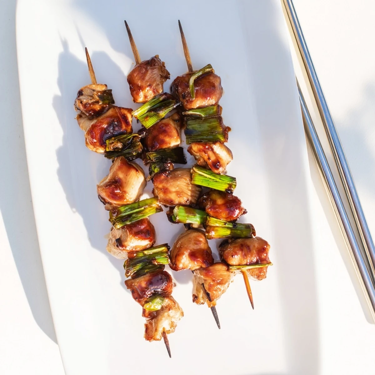 Juicy Japanese Chicken Yakitori skewers on a platter, glistening with tare glaze and perfect for sharing.