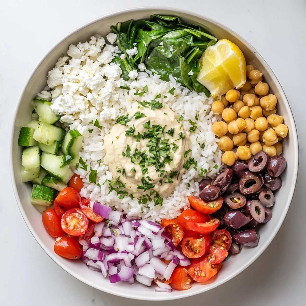 Colorful Mediterranean rice bowl topped with crisp vegetables, hummus, and zesty lemon-tahini drizzle