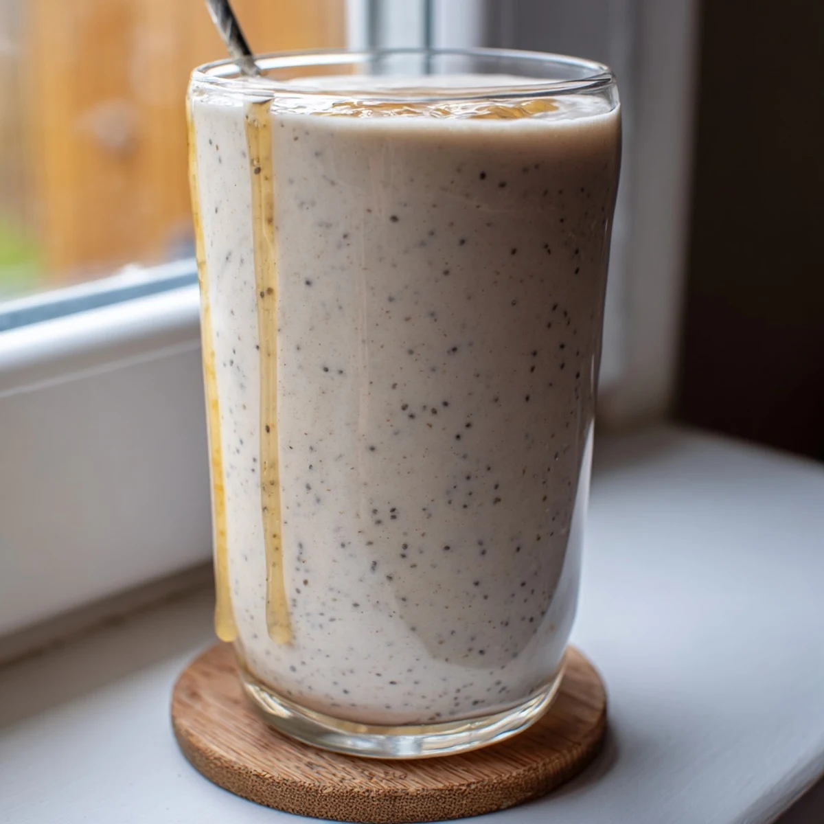 Golden Greek yogurt banana smoothie blended smooth with ice in clear glasses on wooden table