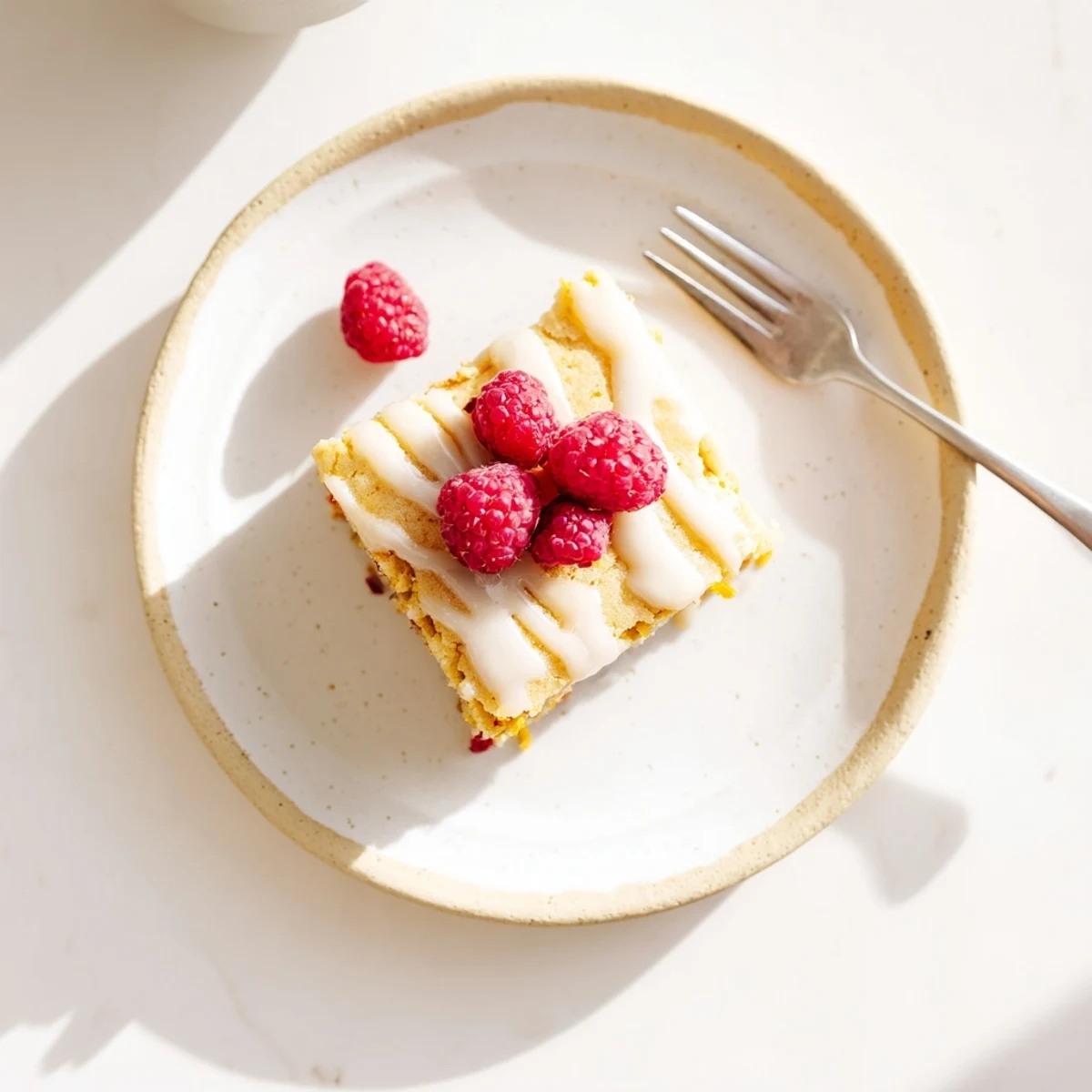 Golden glazed raspberry lemon blondies topped with zesty white drizzle and fresh berry garnish