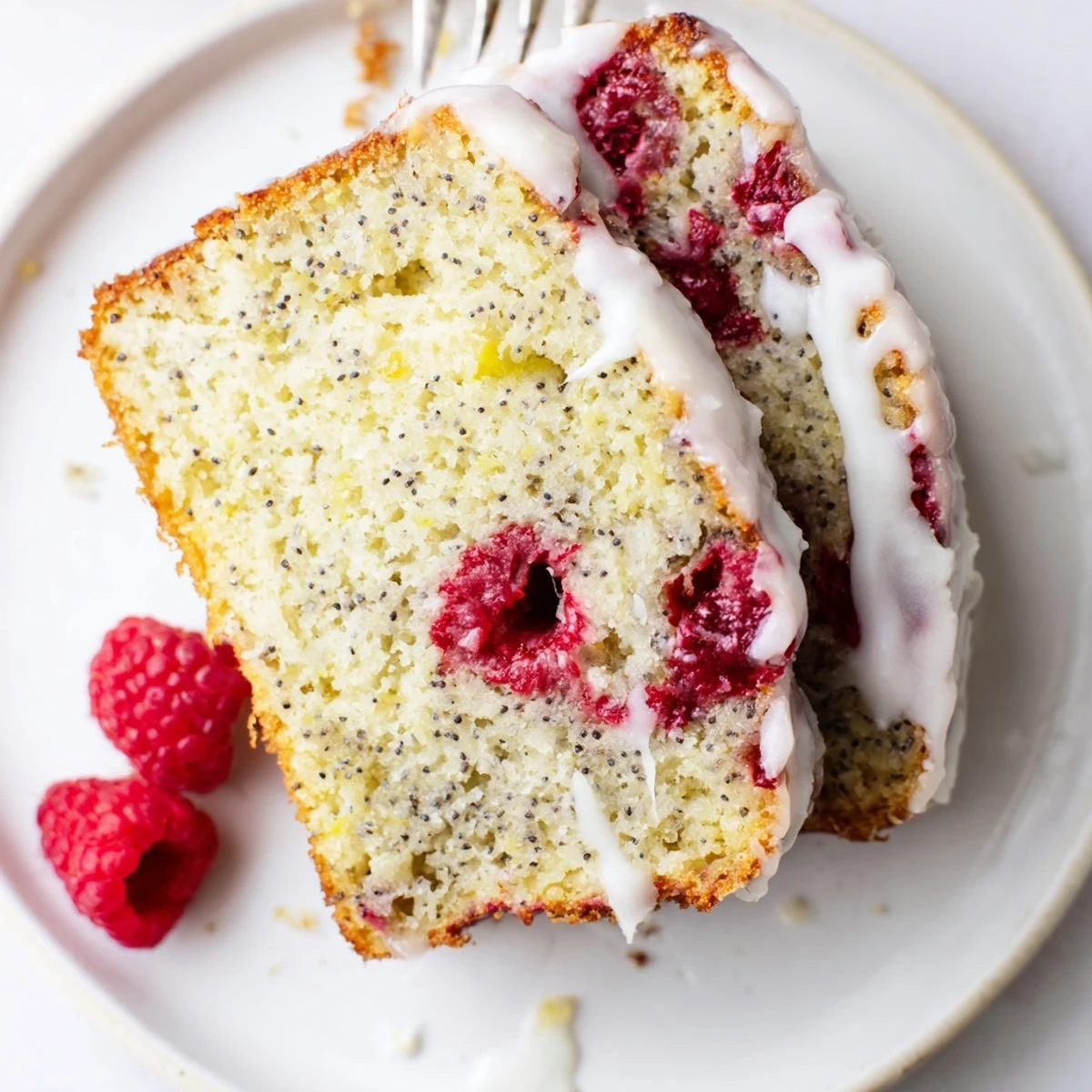 Golden raspberry lemon poppyseed loaf cake drizzled with white lemon glaze on a white serving plate.