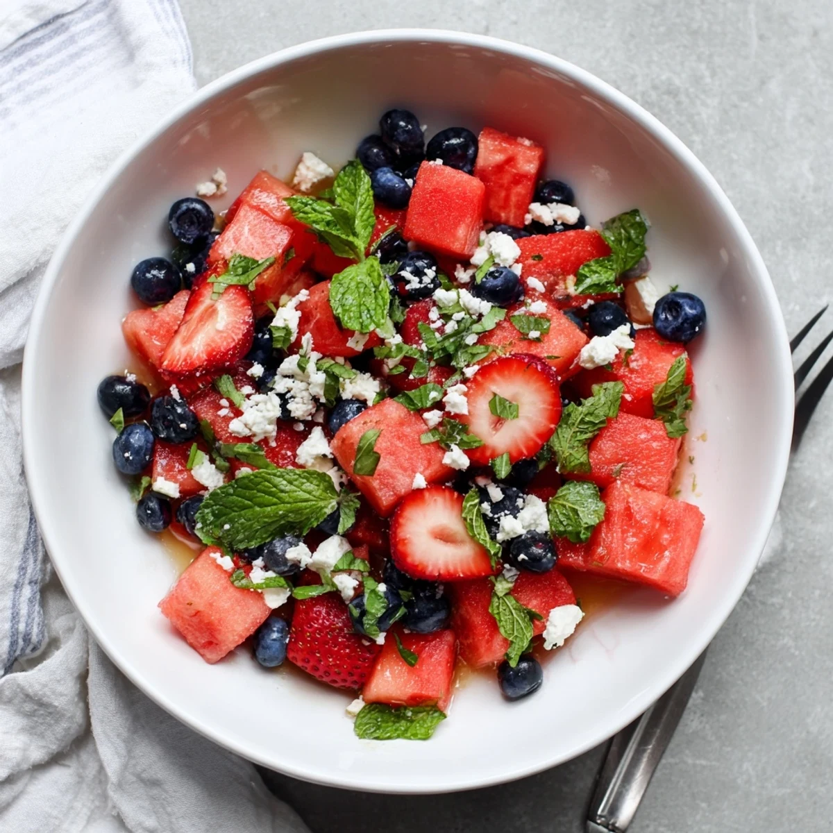 Colorful bowl of strawberry watermelon salad topped with mint leaves and tangy honey lime dressing.