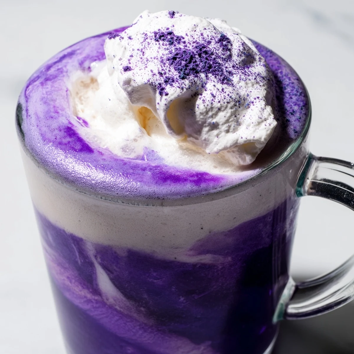 Vibrant purple ube latte topped with whipped cream in a clear glass