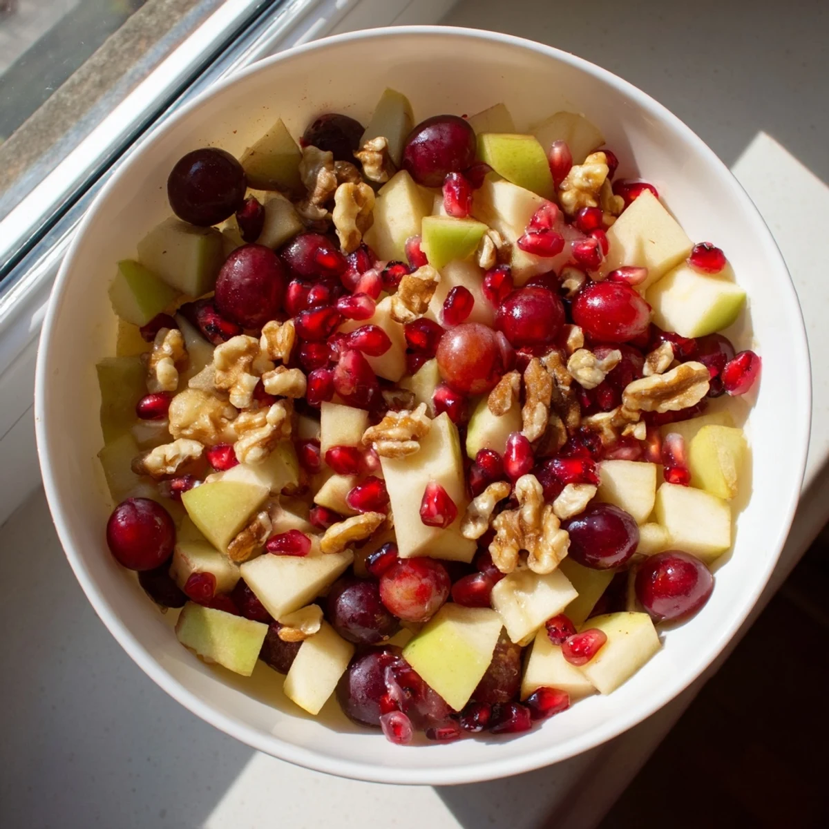 Colorful bowl of minute fall fruit salad featuring diced apples, pears, pomegranate arils, and walnuts drizzled with citrus-honey dressing