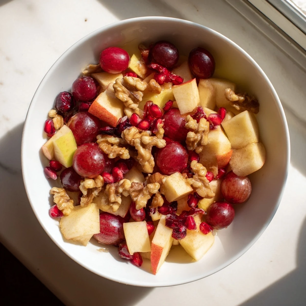 Vibrant glass serving dish filled with quick fall fruit salad tossed in orange honey dressing and sprinkled with pomegranate seeds