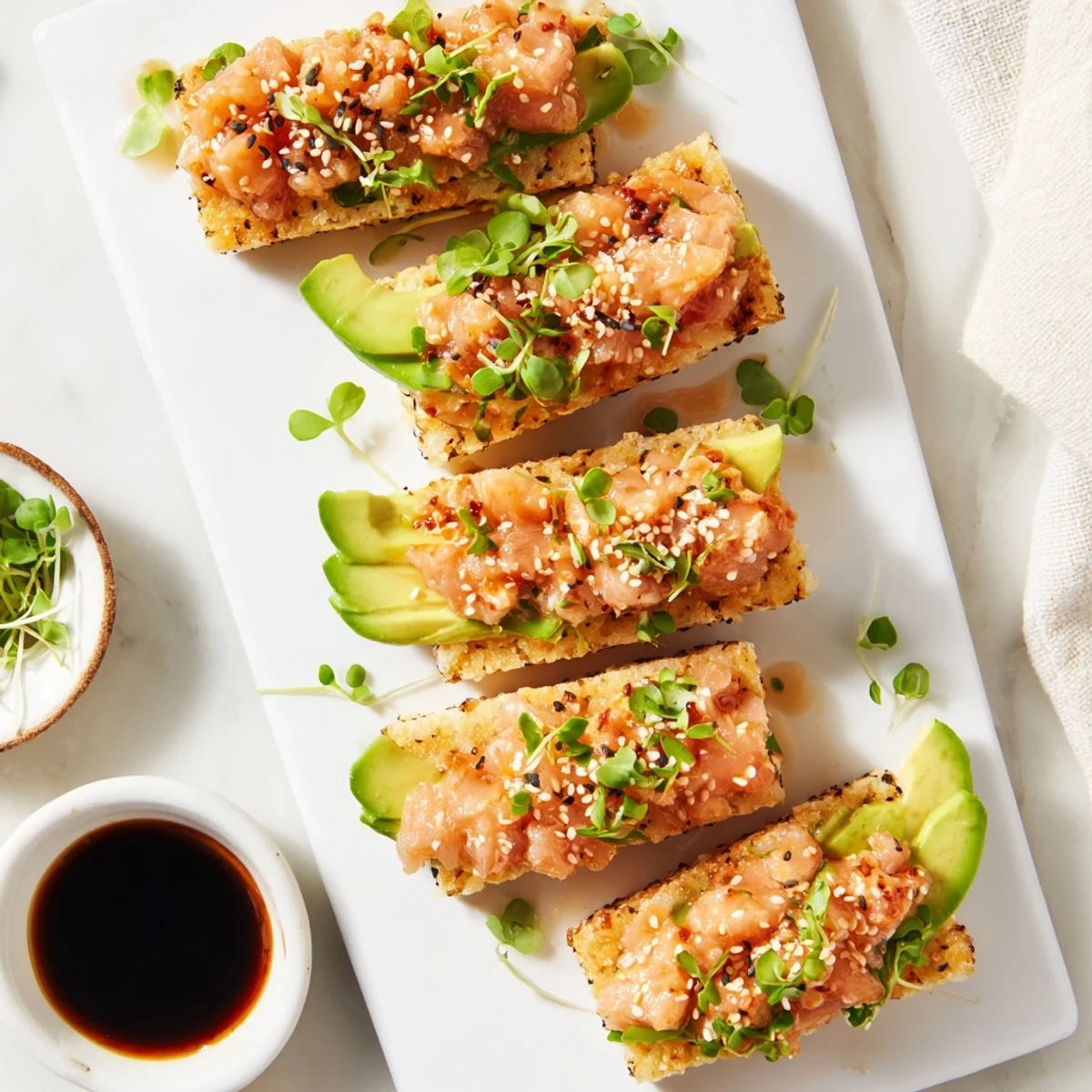 Appetizer of pan-fried sushi rice squares crowned with seasoned salmon and creamy avocado
