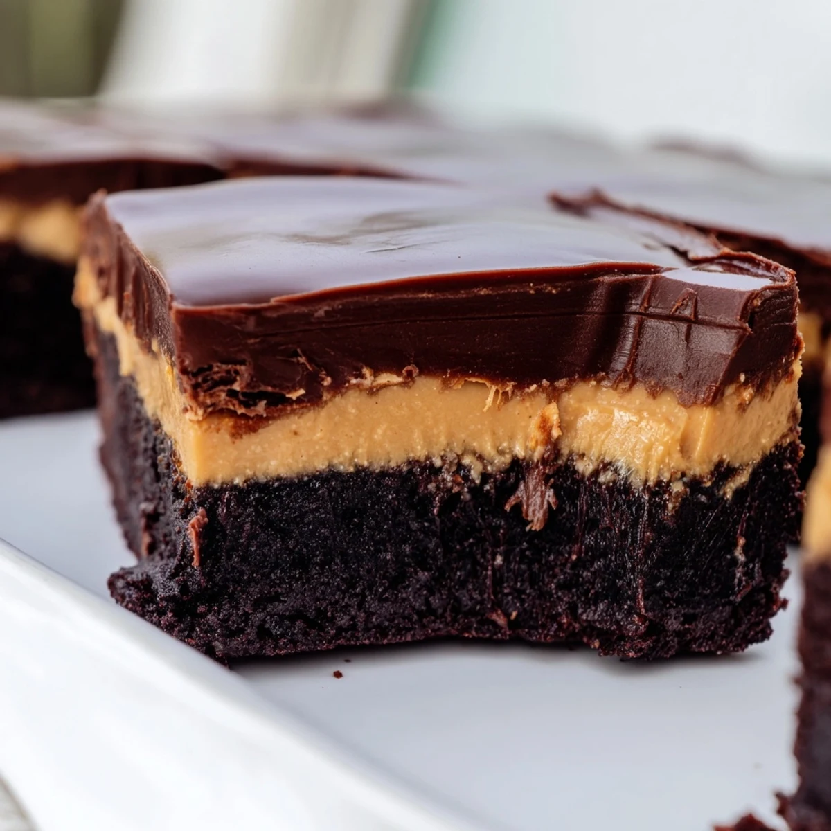 Slice of layered peanut butter brownies showing rich chocolate base topped with creamy peanut butter frosting and glossy ganache