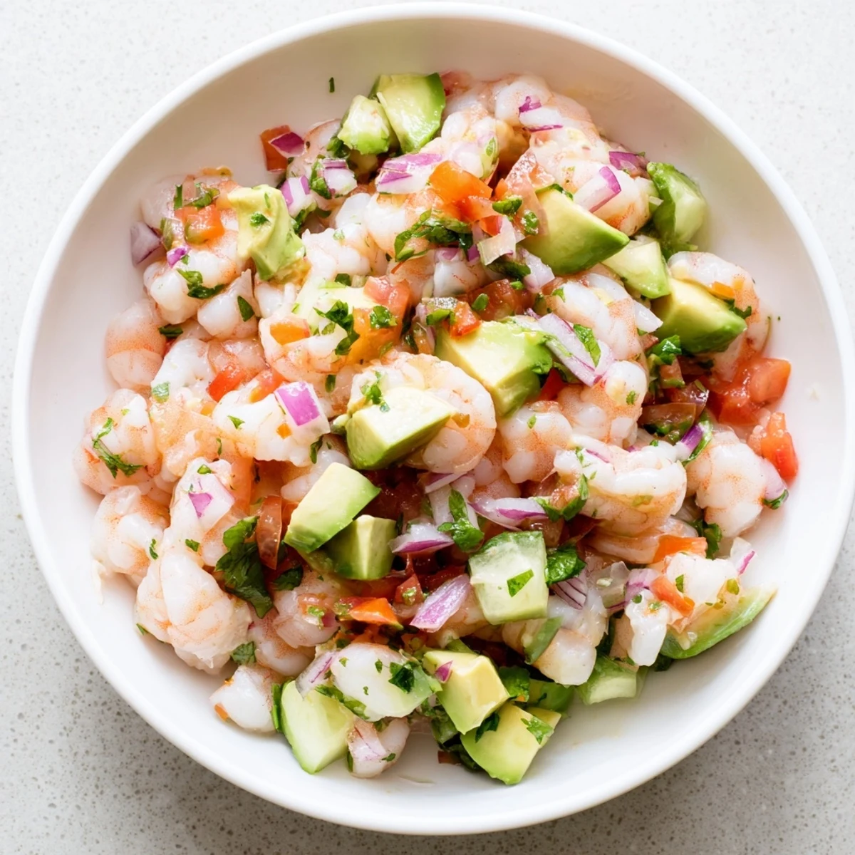 Fresh easy shrimp ceviche served in white bowl with vibrant red onion, green cilantro, and lime wedges