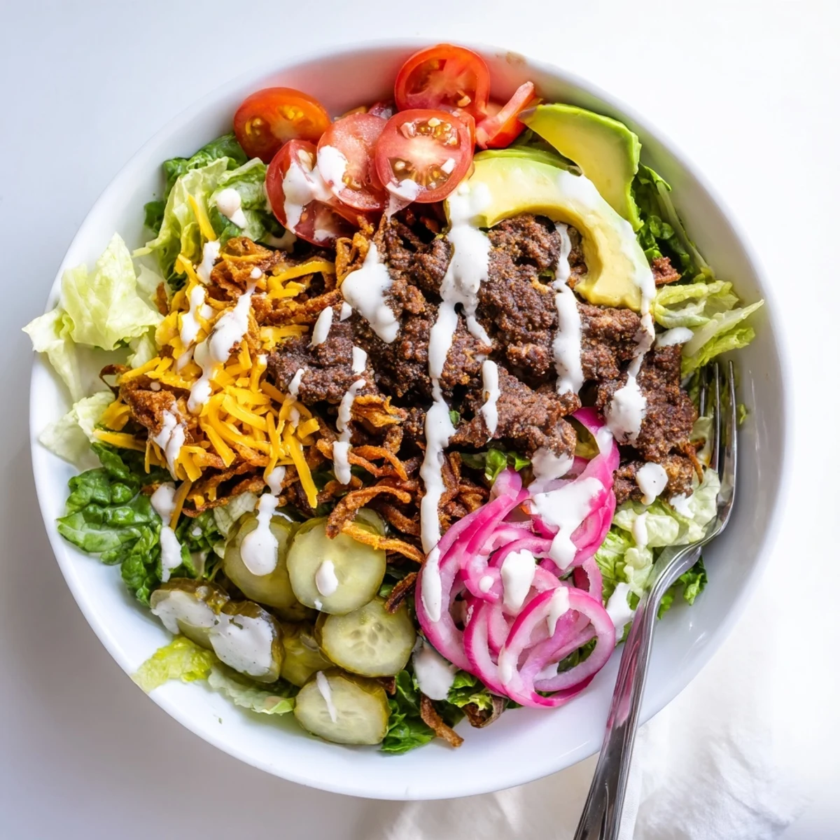 Deconstructed smash burger bowl features seasoned beef crumbles atop romaine with tomatoes pickles avocado and cheddar