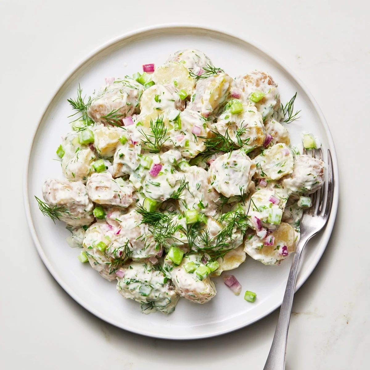 Creamy Greek yogurt potato salad with tender red potatoes and fresh green herbs served in a white bowl