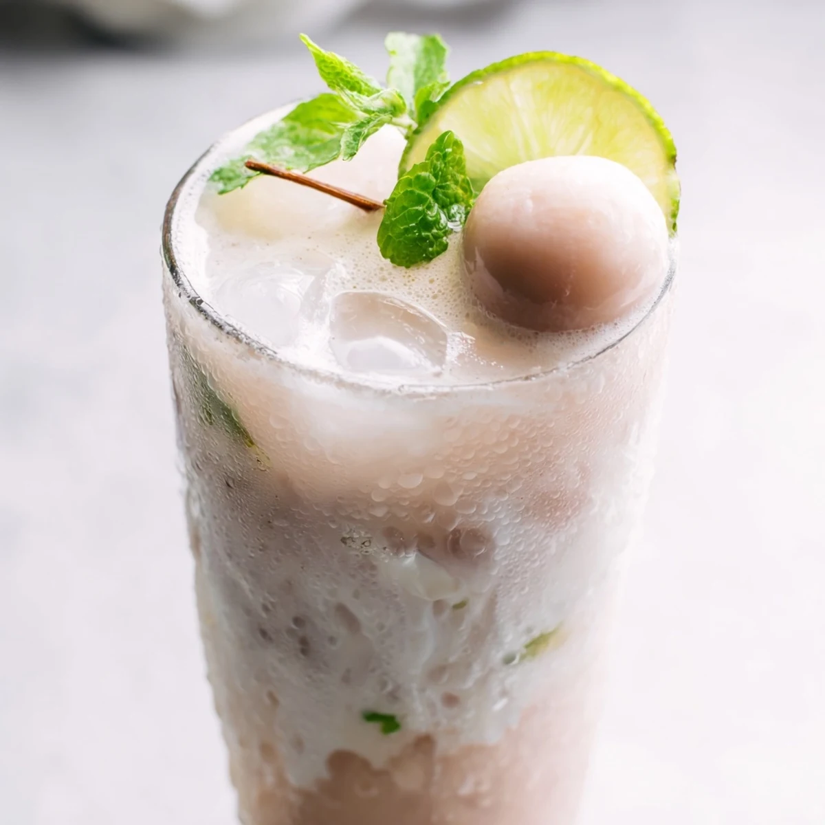 Refreshing coconut lychee iced drink with lime slices and whole lychees floating among ice cubes