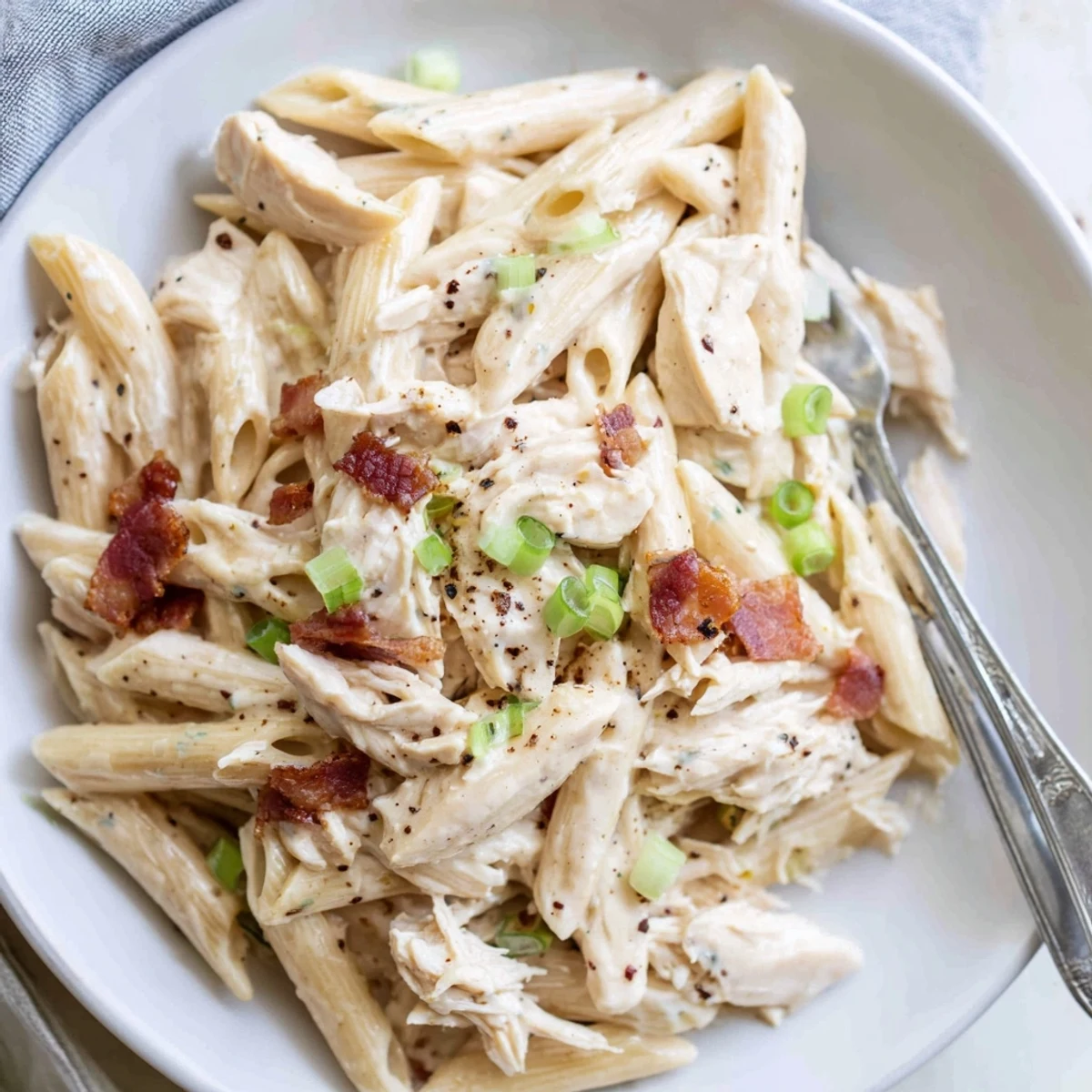 Twirling fork lifts crack chicken pasta with shredded chicken, bacon bits, and green onion garnish