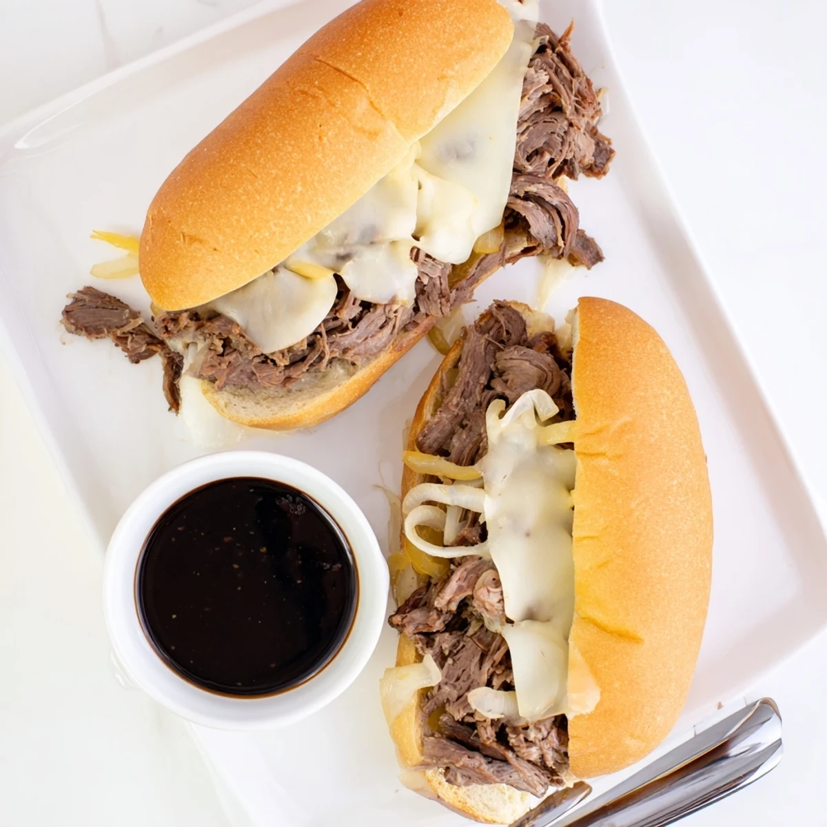 Tender Crockpot French Dip Sandwiches with melted cheese served alongside rich au jus dipping sauce