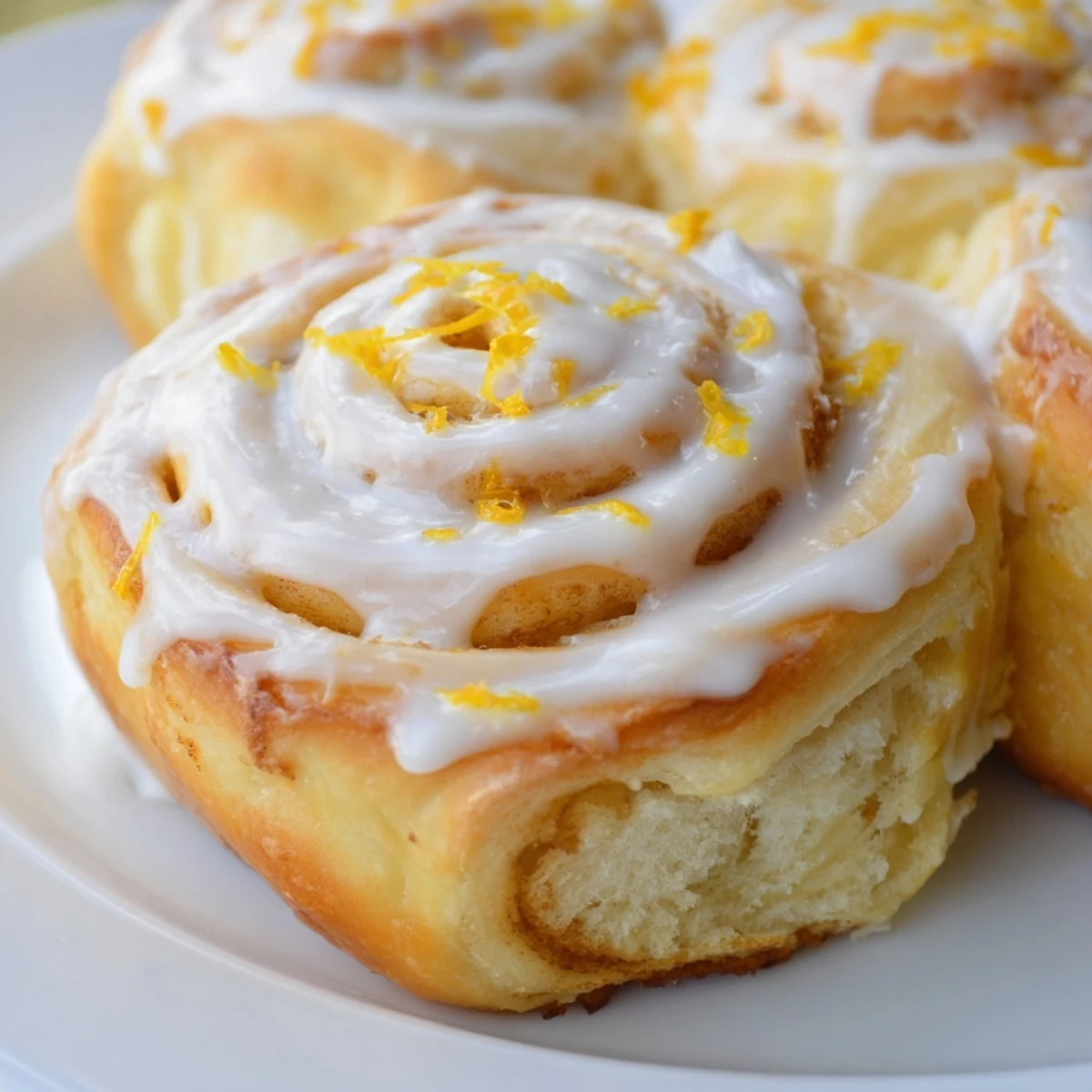 Warm breakfast lemon rolls topped with tangy lemon glaze on a serving plate