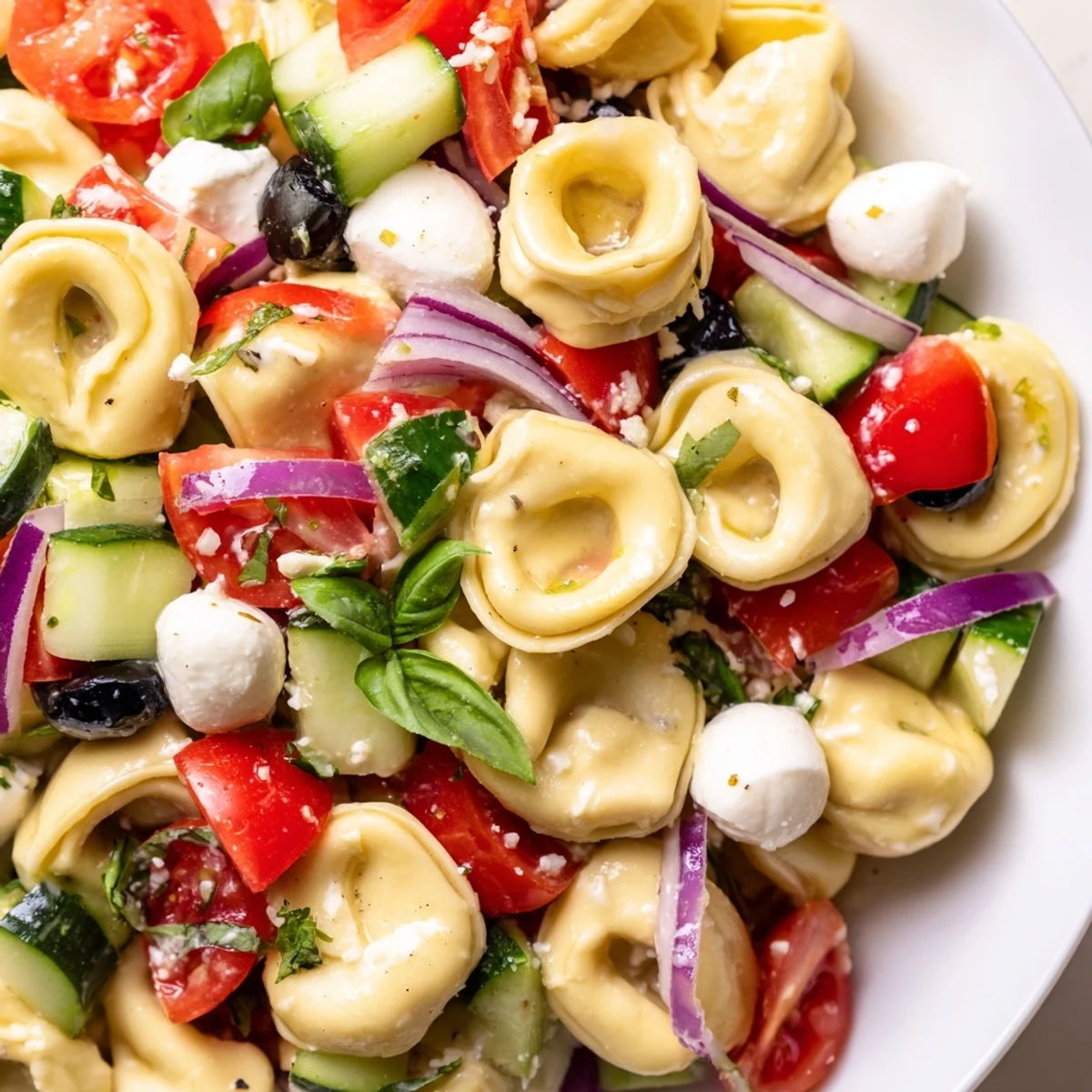 Colorful tortellini salad with cherry tomatoes, cucumber, and zesty Italian dressing in a white bowl