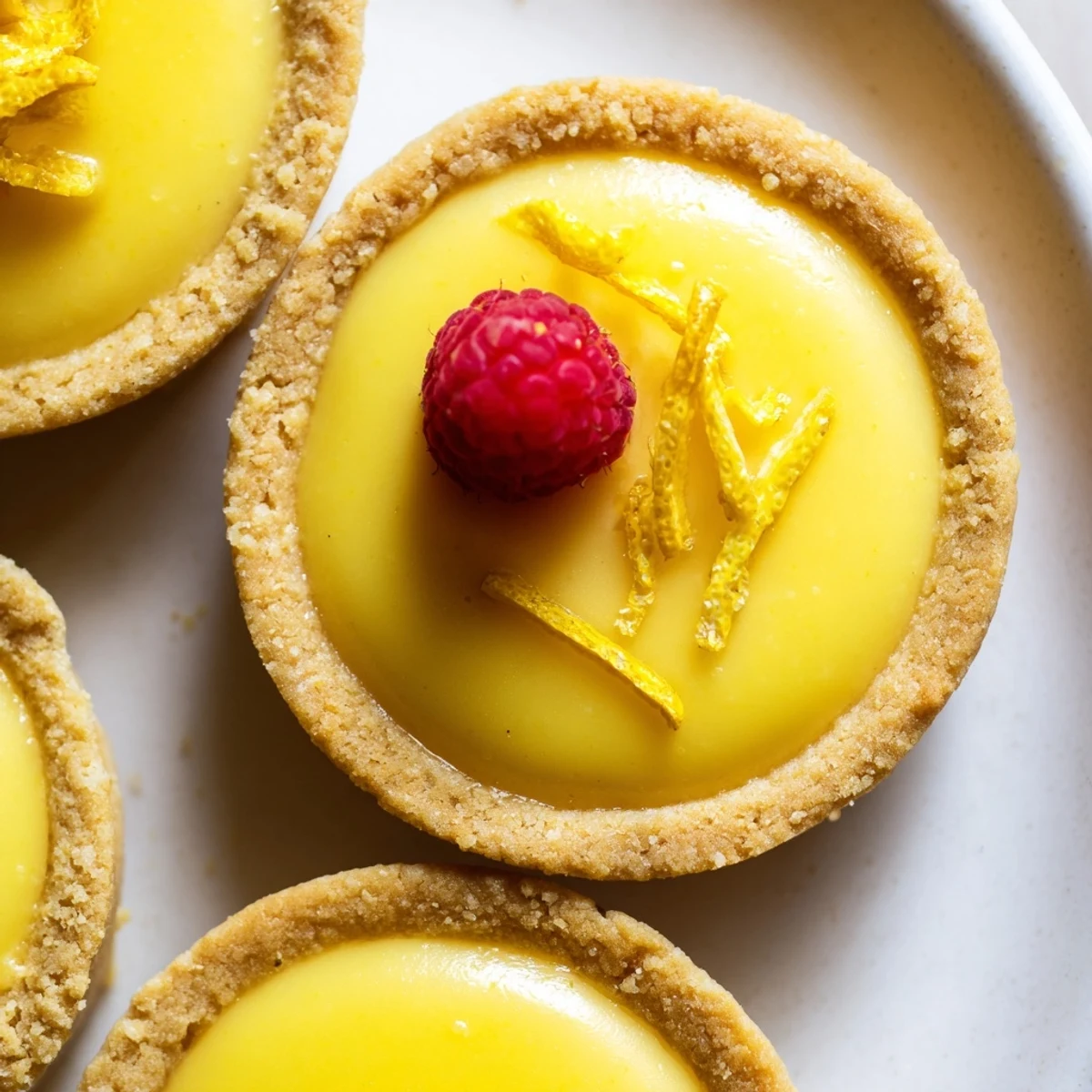 Mini vegan lemon tarts topped with fresh berries on a rustic white serving plate
