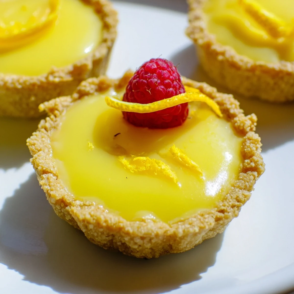 Bright yellow mini vegan lemon tarts garnished with lemon zest and edible flowers indoors