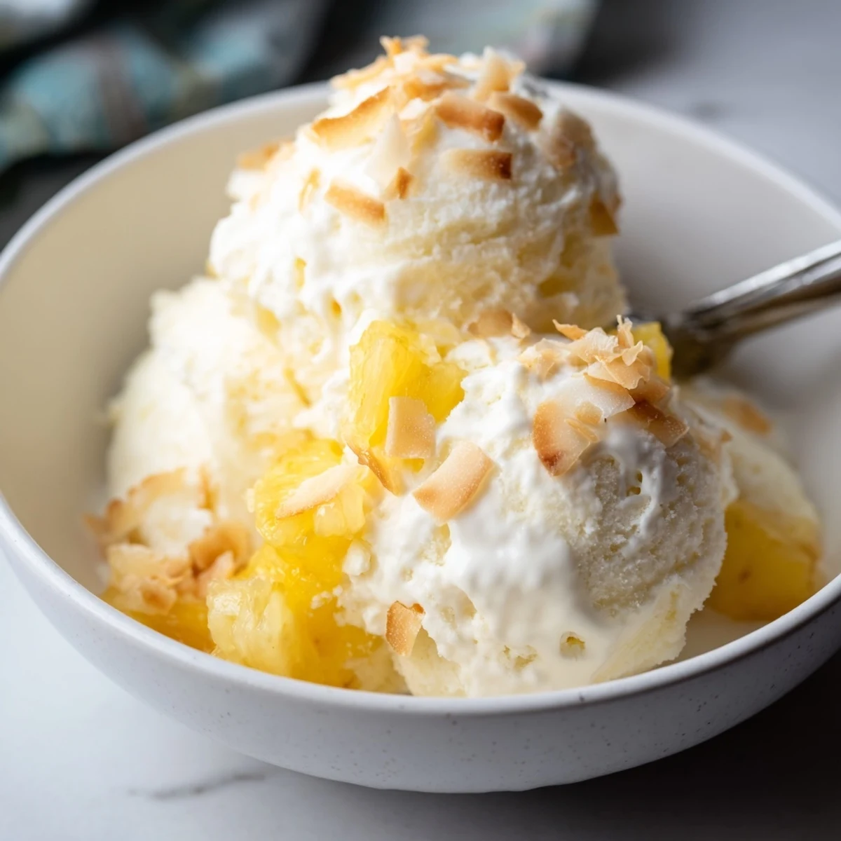Creamy Pineapple Ice Cream crowned with toasted coconut, spoon melting glossy swirls