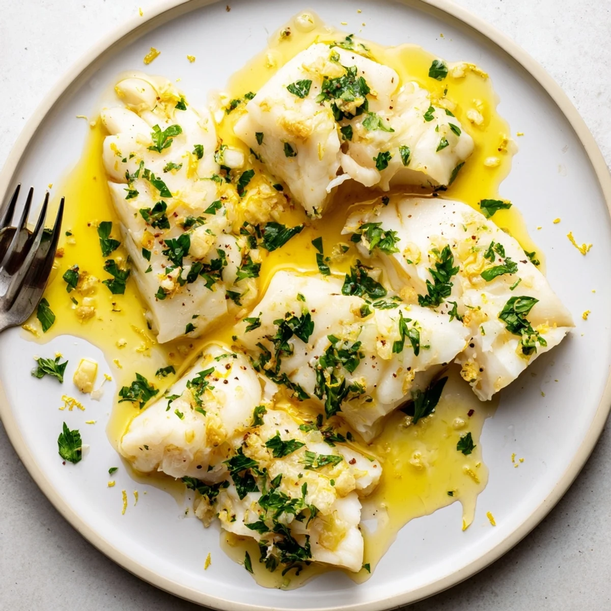 Flaky white fish simmered in tangy lemon garlic butter with parsley garnish on a white plate